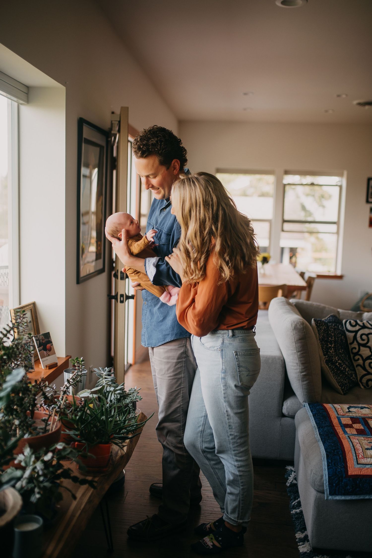 Young couple admiring their newborn baby together in a cozy sunlit living room.