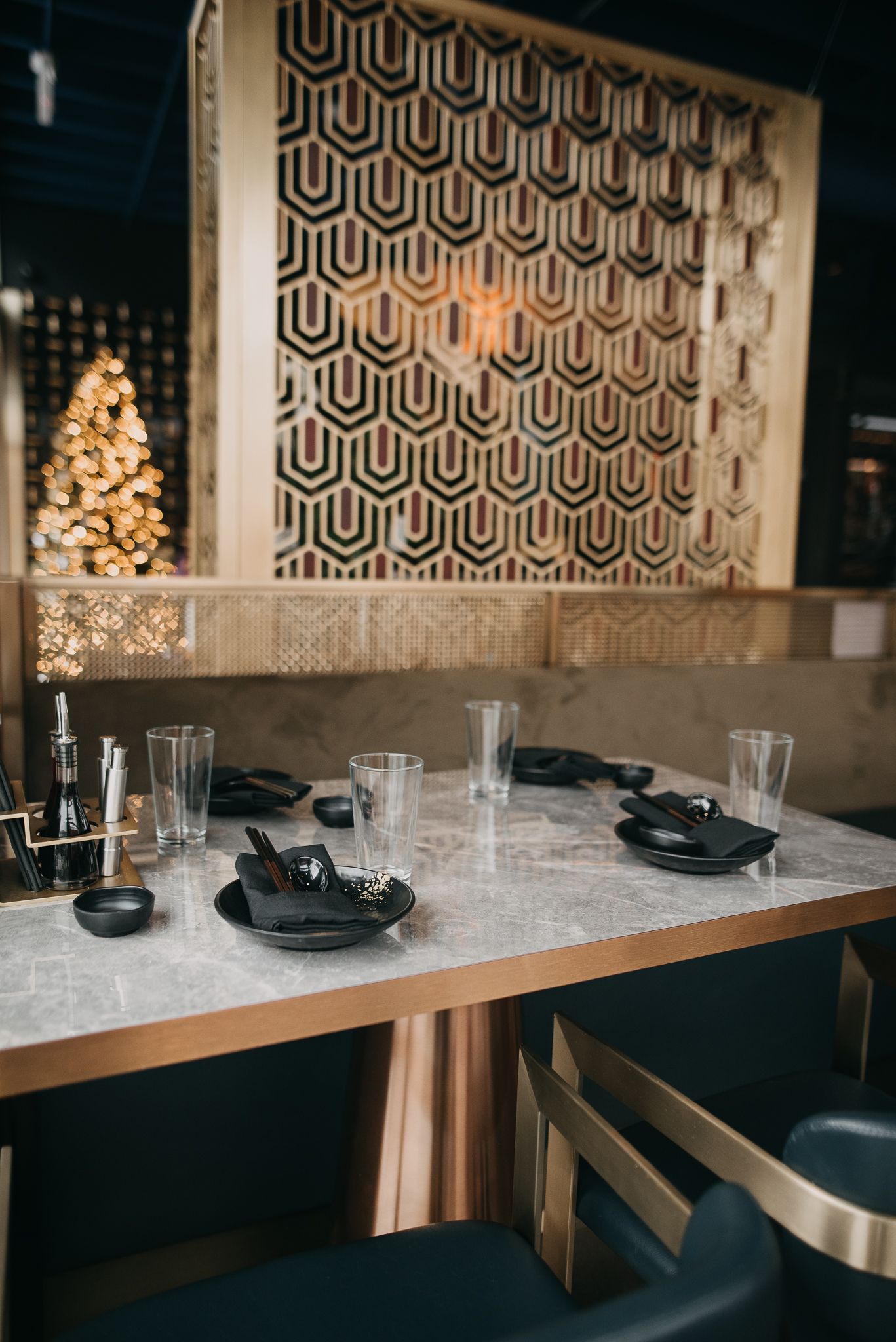 Upscale restaurant dining table set with black plates and glasses against a geometric gold wall.
