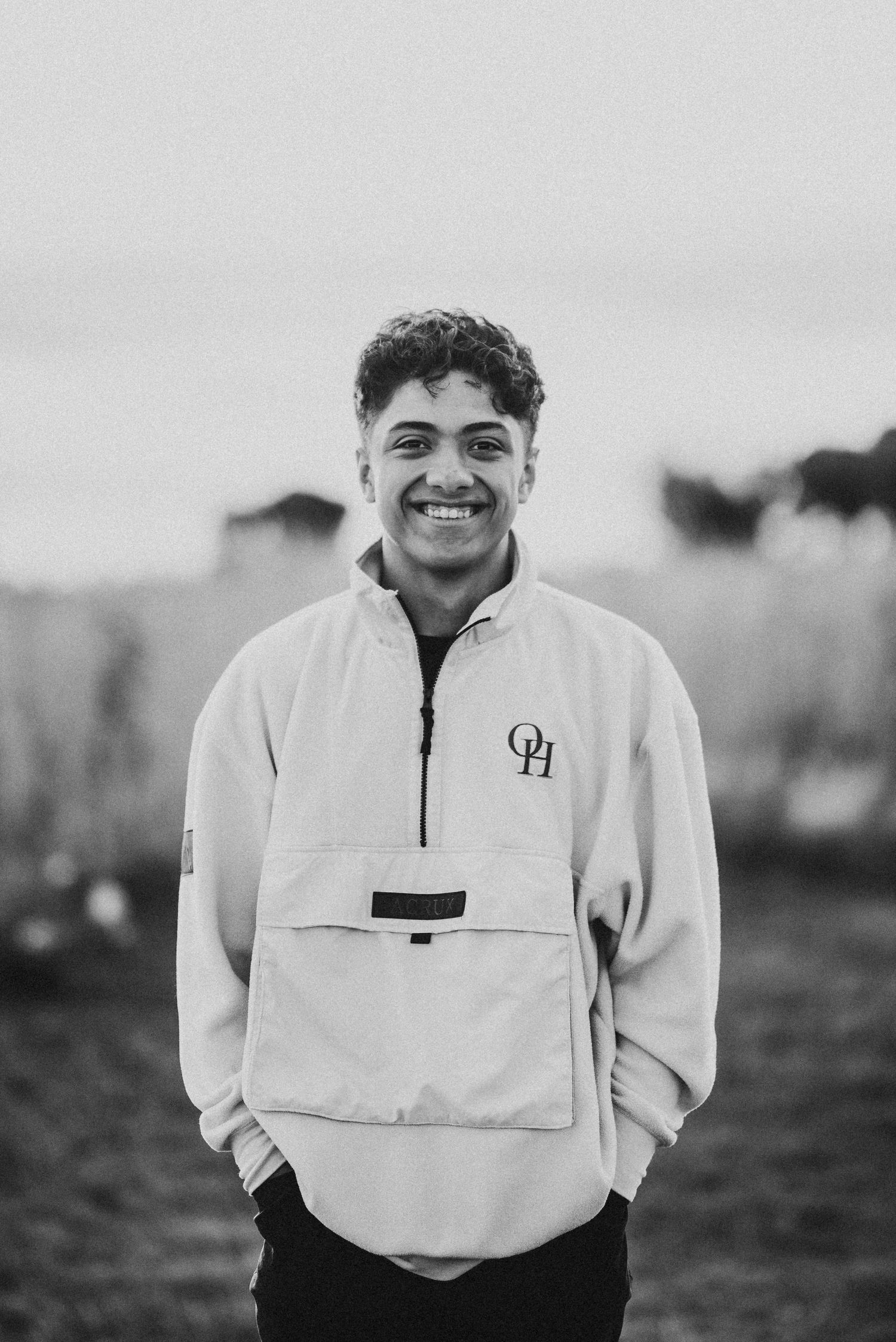 Smiling young man in black and white photo wearing OH pullover sweatshirt in open field.
