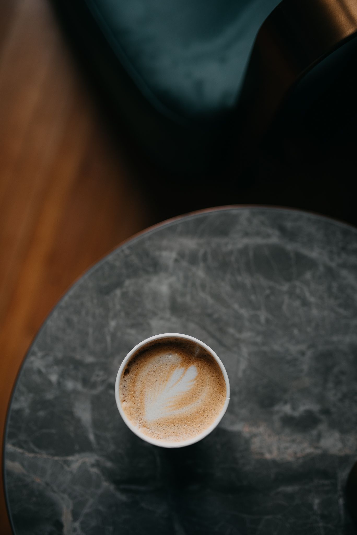 Artisan latte with leaf latte art in a white cup on a gray marble table.