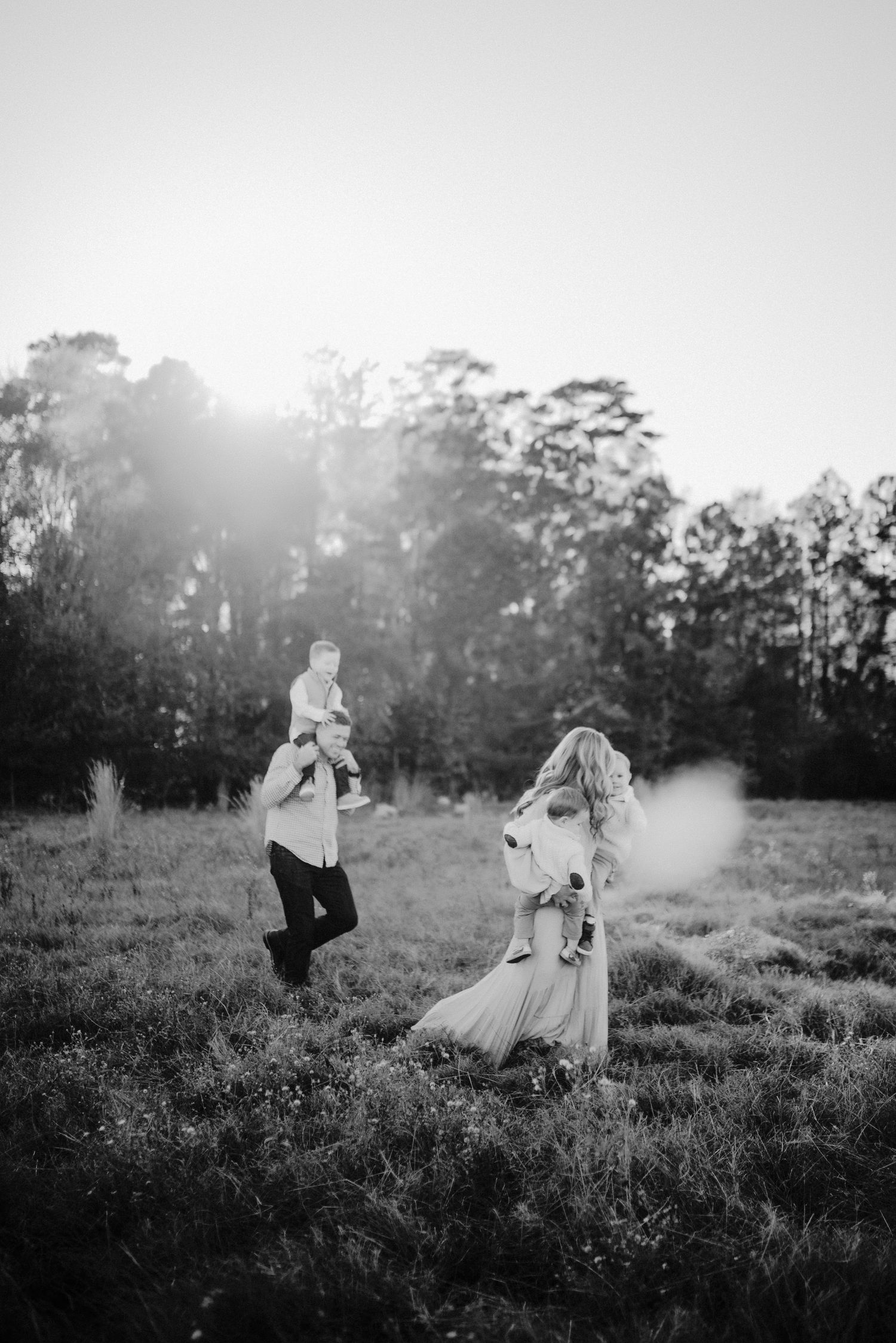 Black and white photo of parents playing with two young children in sunlit open field.