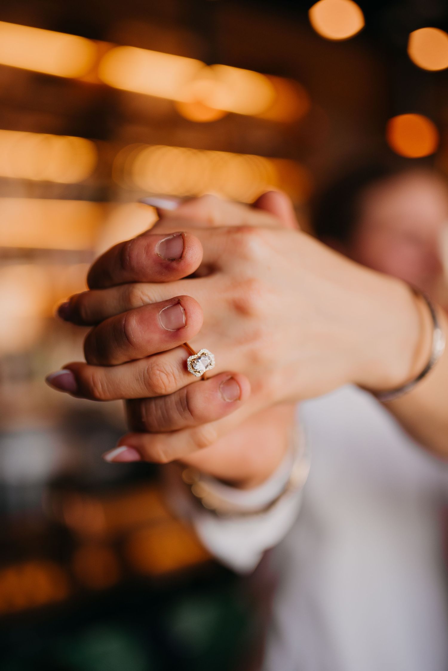Close-up of couple holding hands displaying a stunning cushion-cut diamond engagement ring in gold.