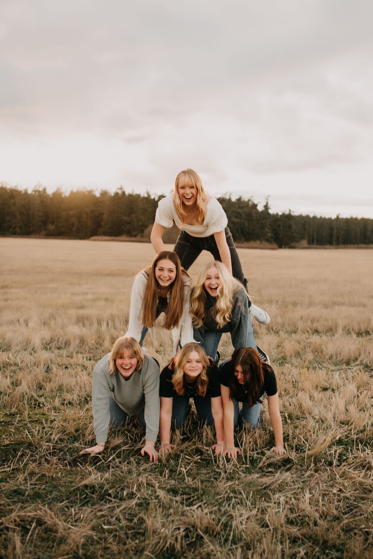 Six teenage girls form a human pyramid in an open field at sunset during friend photoshoot.