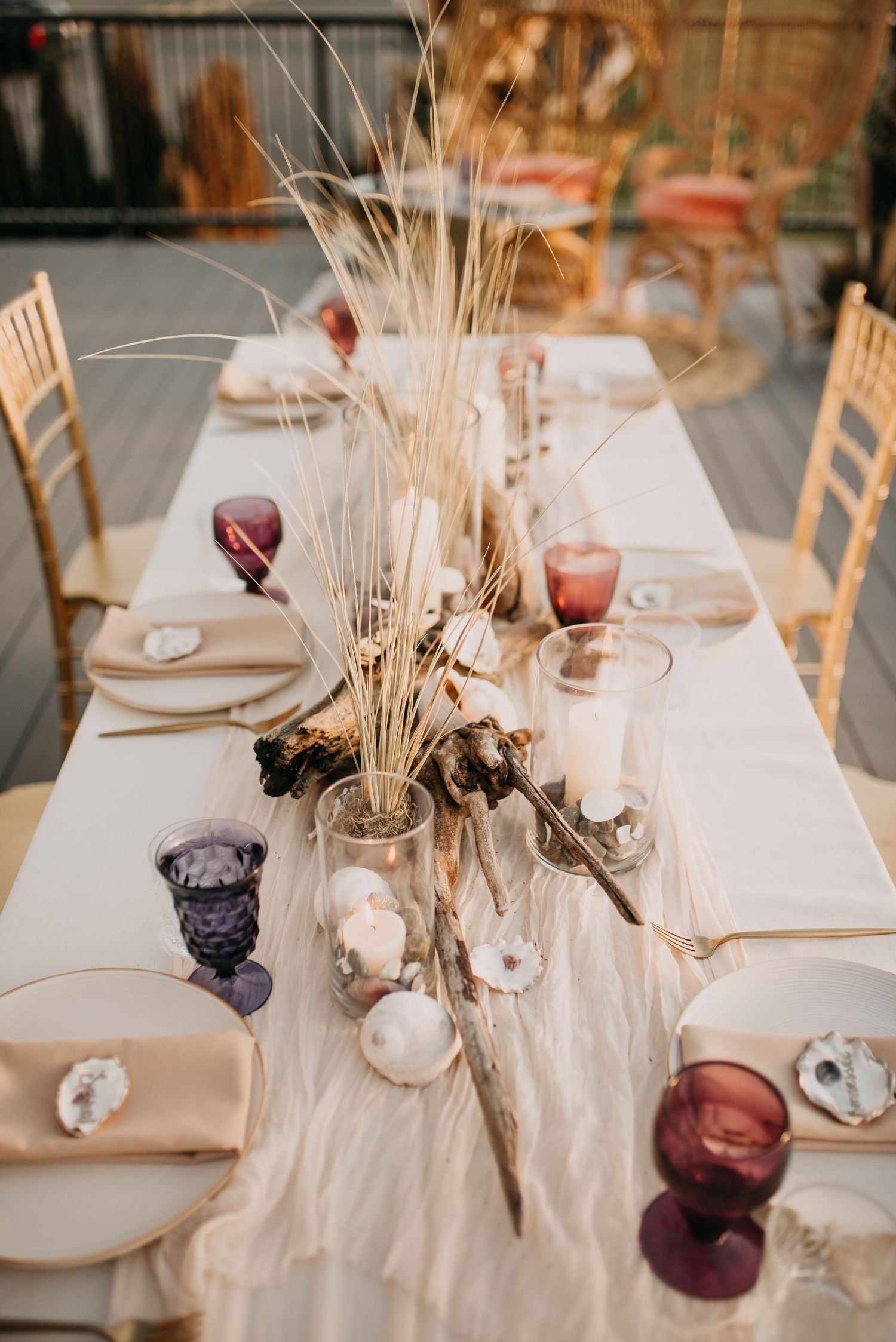 Elegant wedding tablescape with driftwood, dried grasses, shells, purple goblets, and gold chairs.