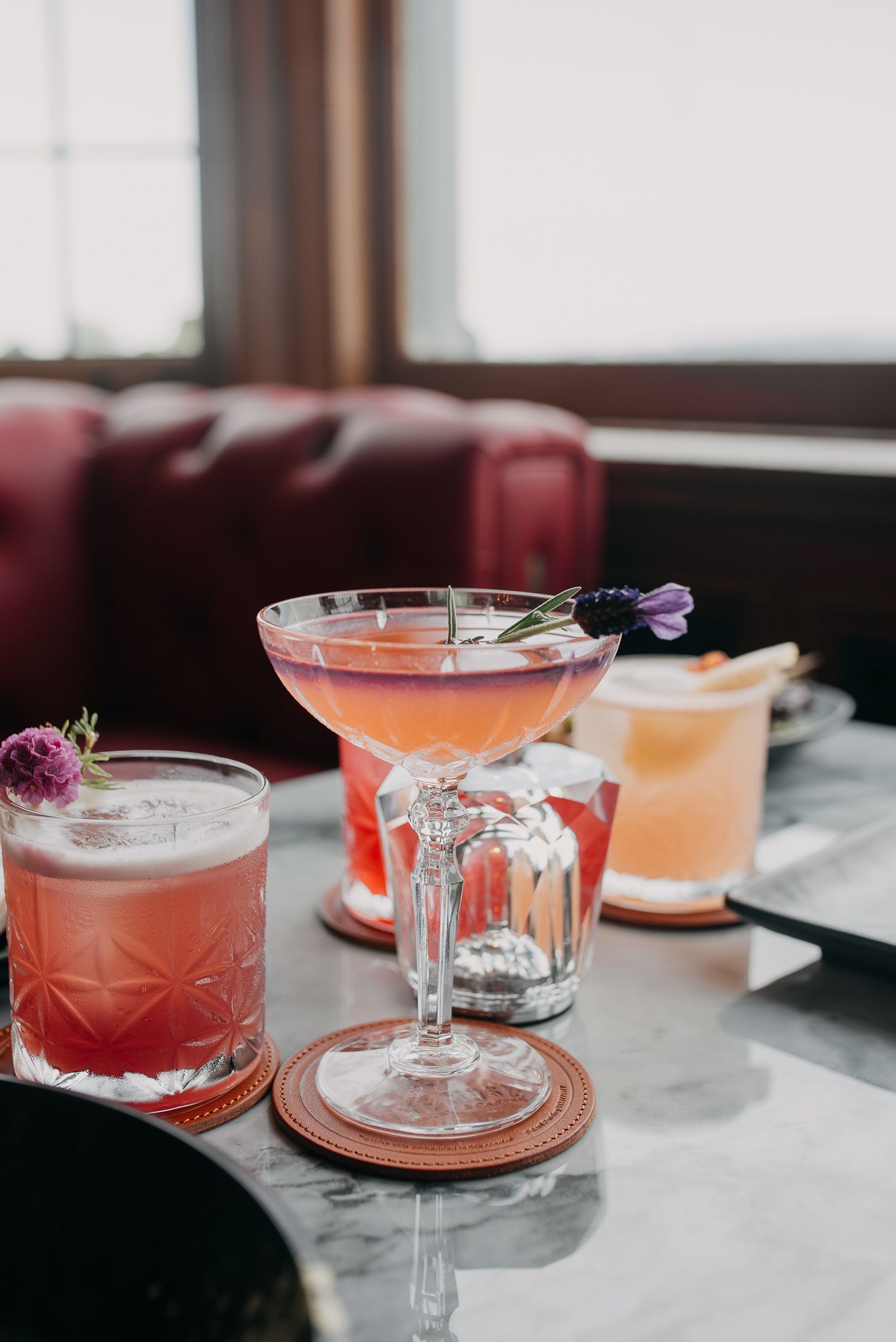Elegant cocktails with floral garnishes served on a marble table in a upscale bar setting.