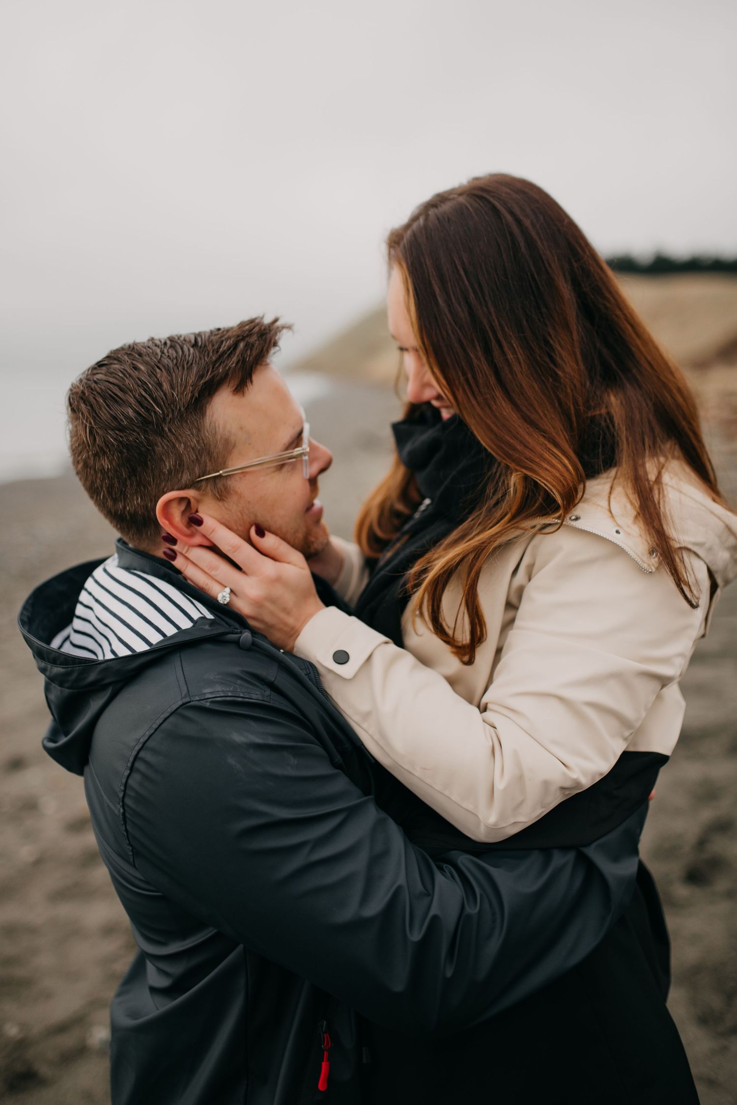 Loving couple gazes at each other on a cloudy beach, woman holding mans face.