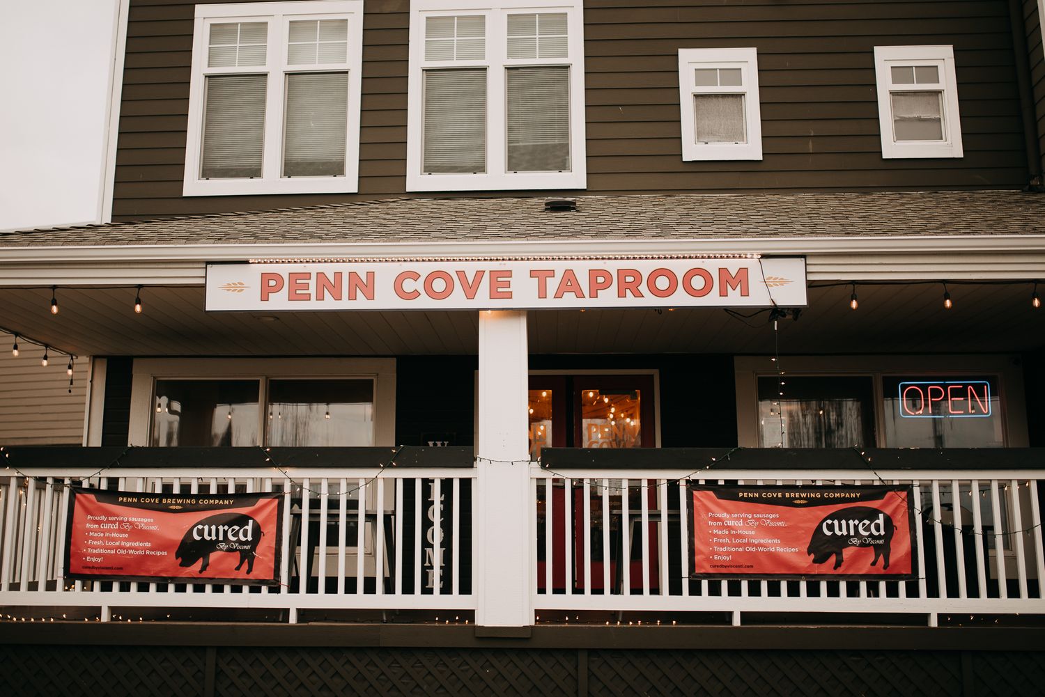 The exterior of Penn Cove Taproom with red banners and a welcoming porch in a charming building.