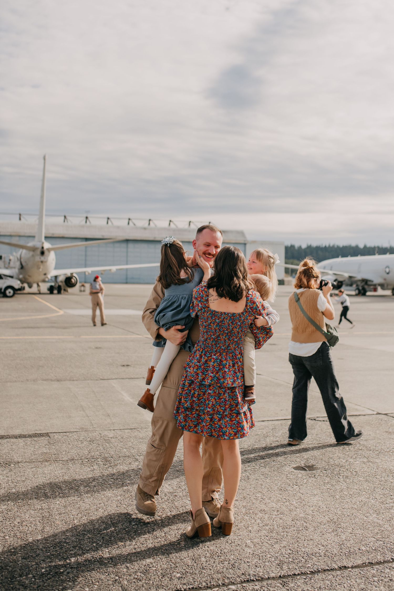 Joyful military homecoming reunion on airport tarmac with family embracing.