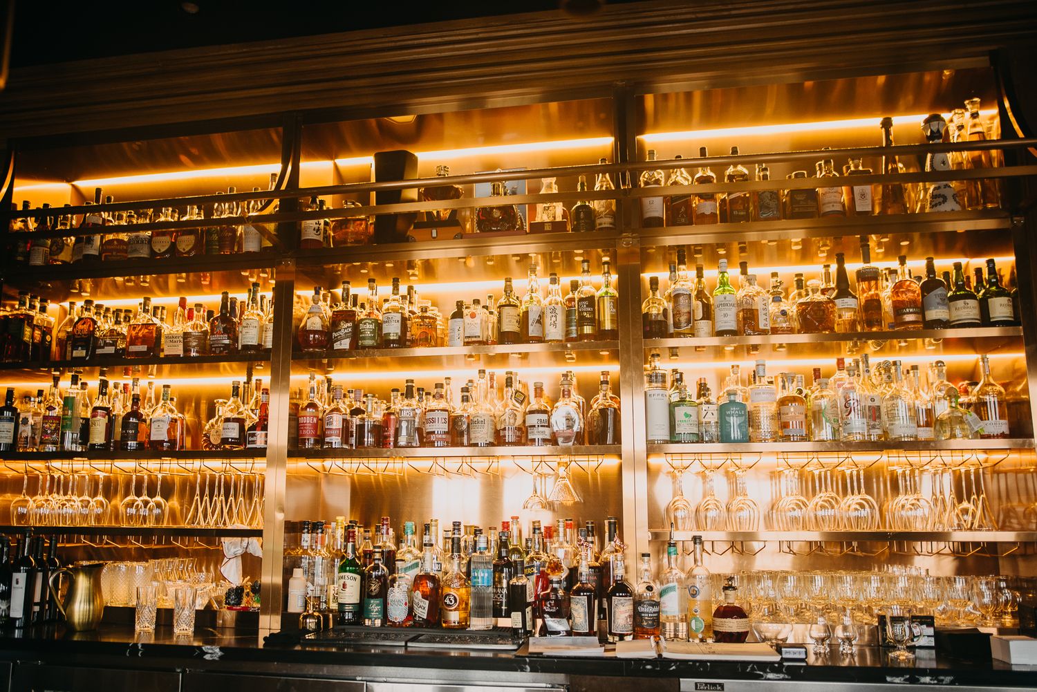 Warmly lit bar shelves stocked with an extensive collection of spirits and glassware.