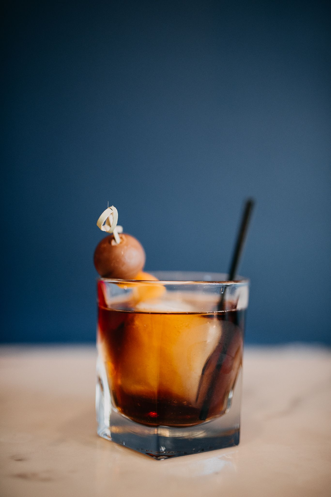 Classic Old Fashioned cocktail with cherry garnish and orange peel in a rocks glass on marble bar.