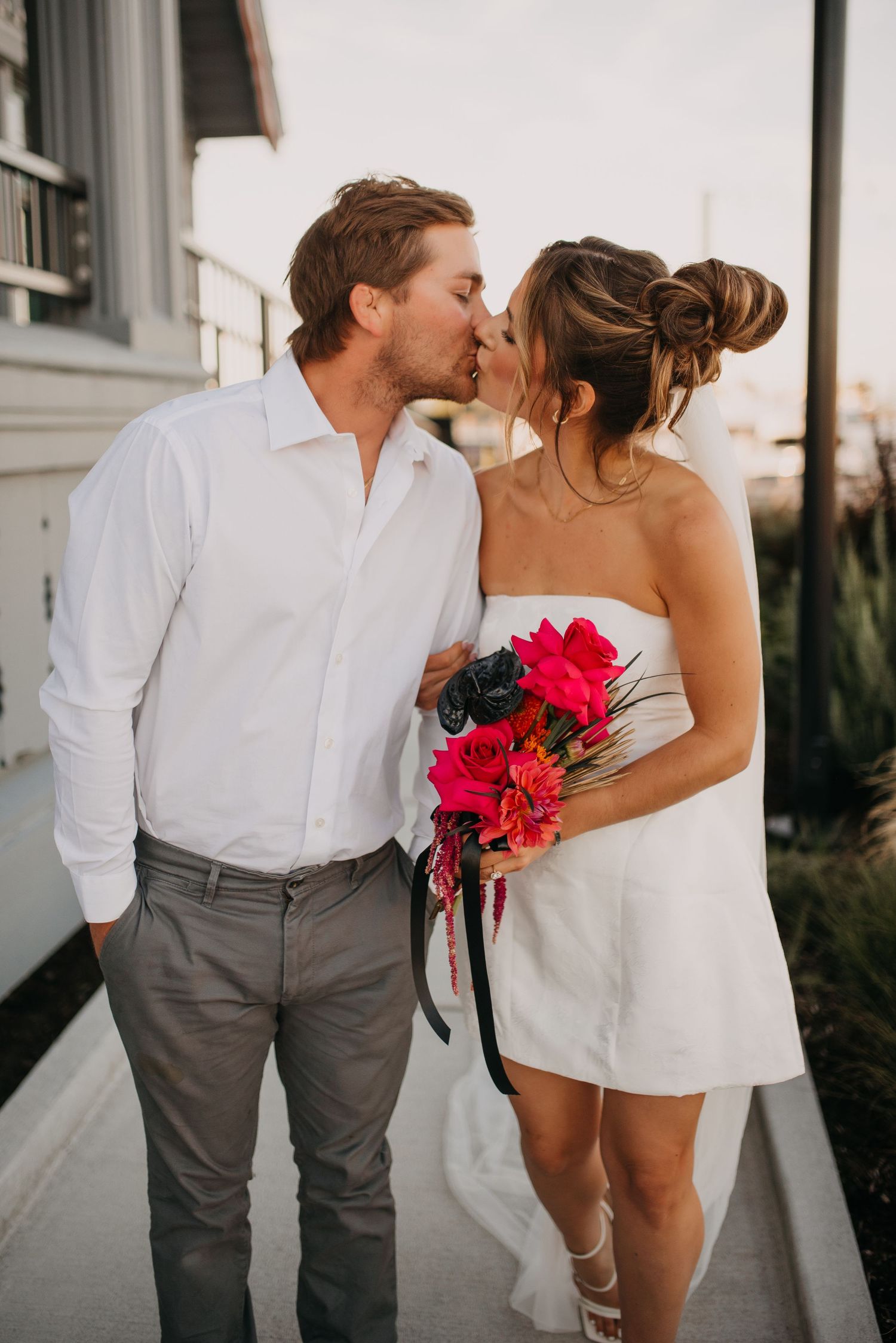 Bride and groom sharing a kiss outdoors, bride holding a vibrant pink tropical flower bouquet.