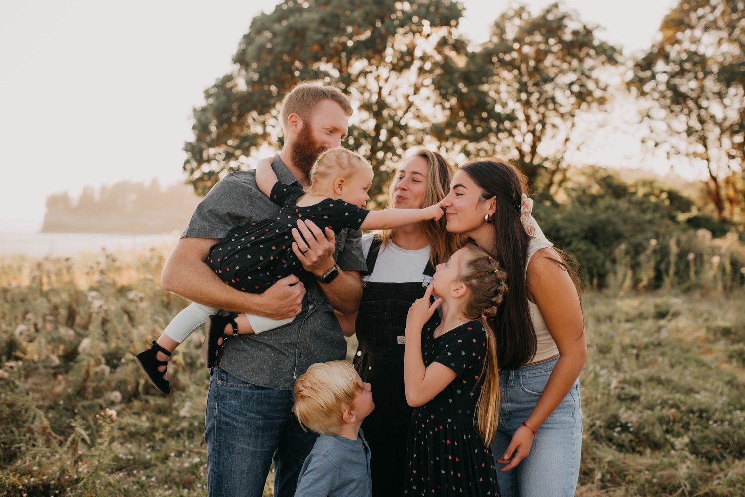 Joyful family of four with two young children sharing kisses and hugs outdoors at golden hour.