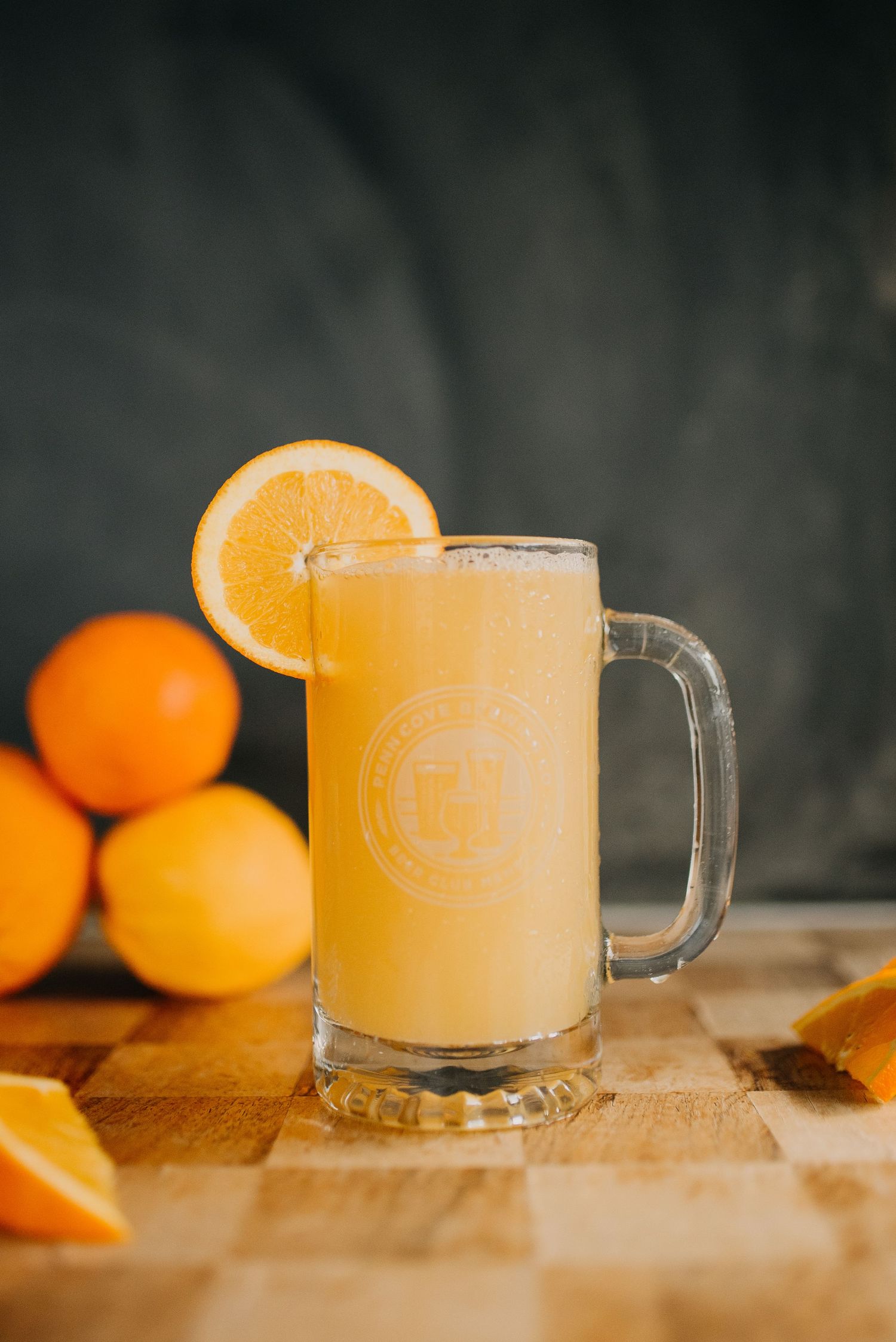 A refreshing orange juice smoothie in a branded glass mug garnished with an orange slice on a wooden cutting board.