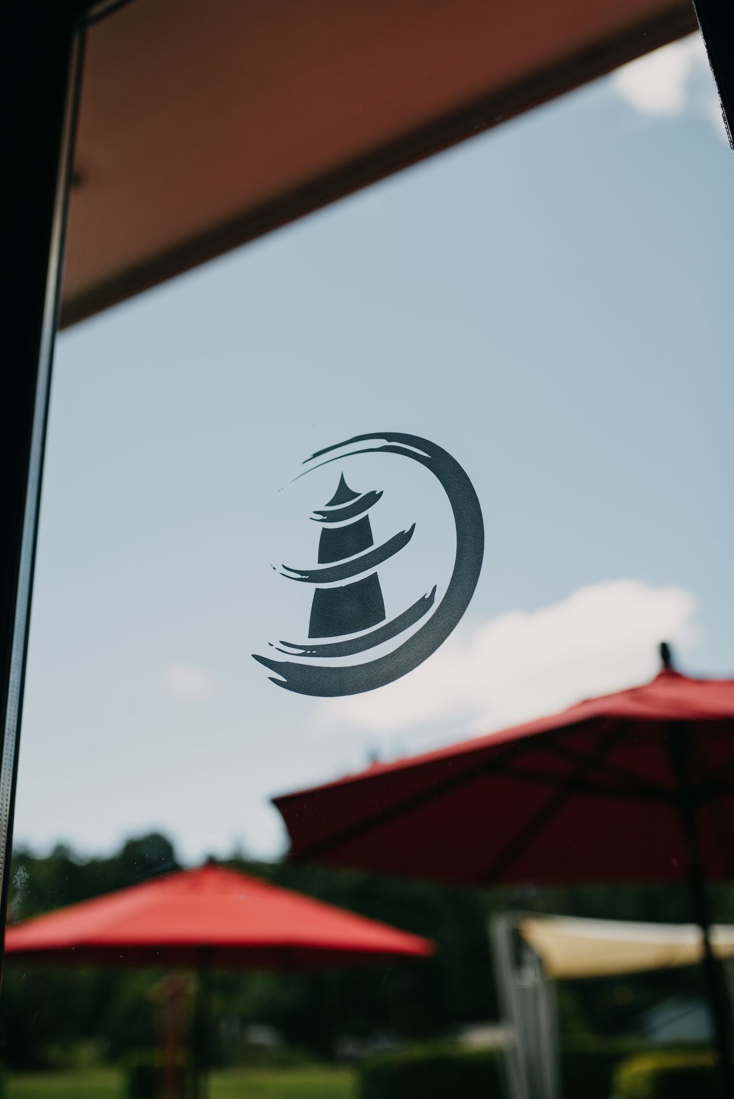 Lighthouse logo decal on glass window with red patio umbrellas in background.