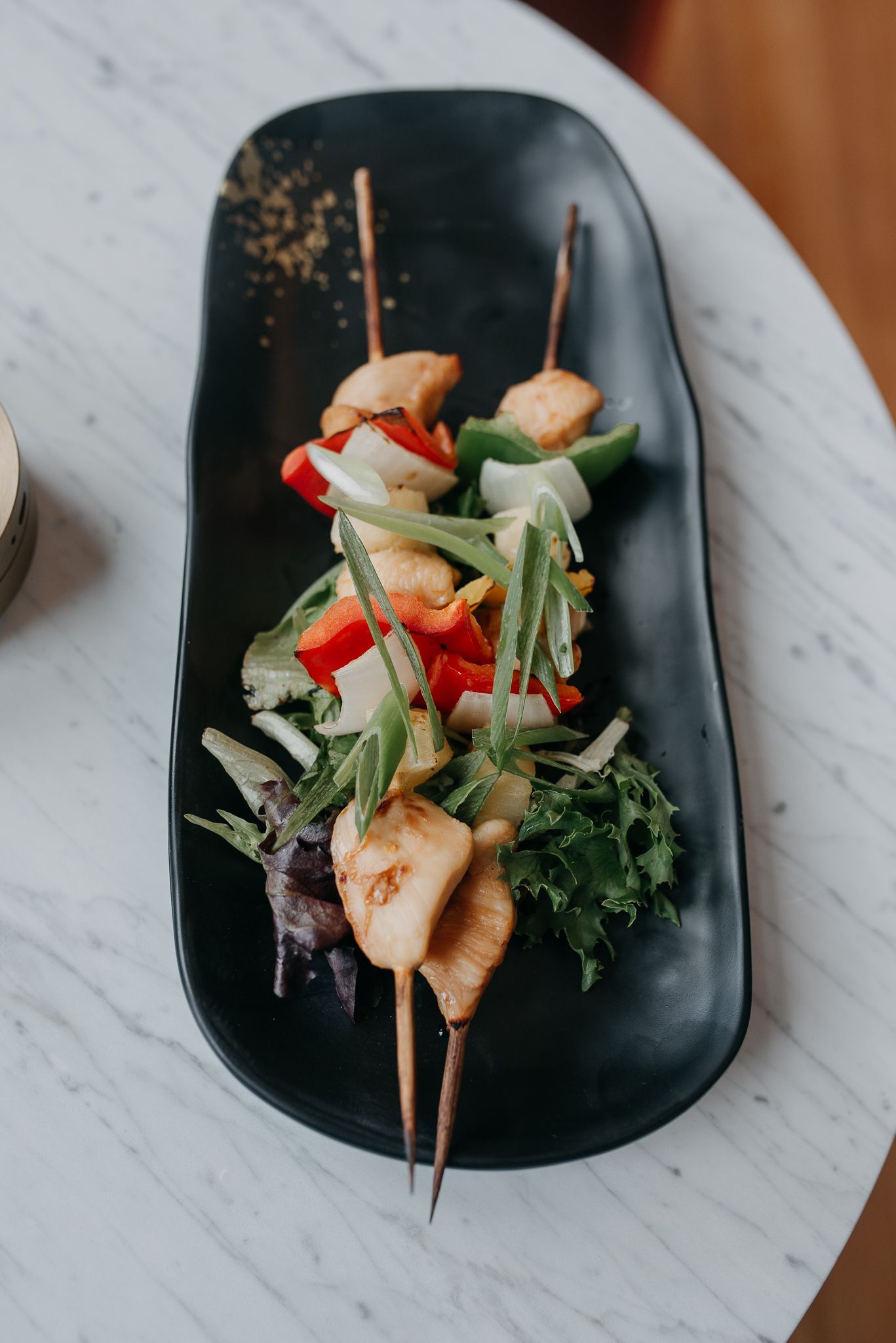 Grilled chicken skewers with colorful bell peppers and fresh greens served on a black ceramic plate.