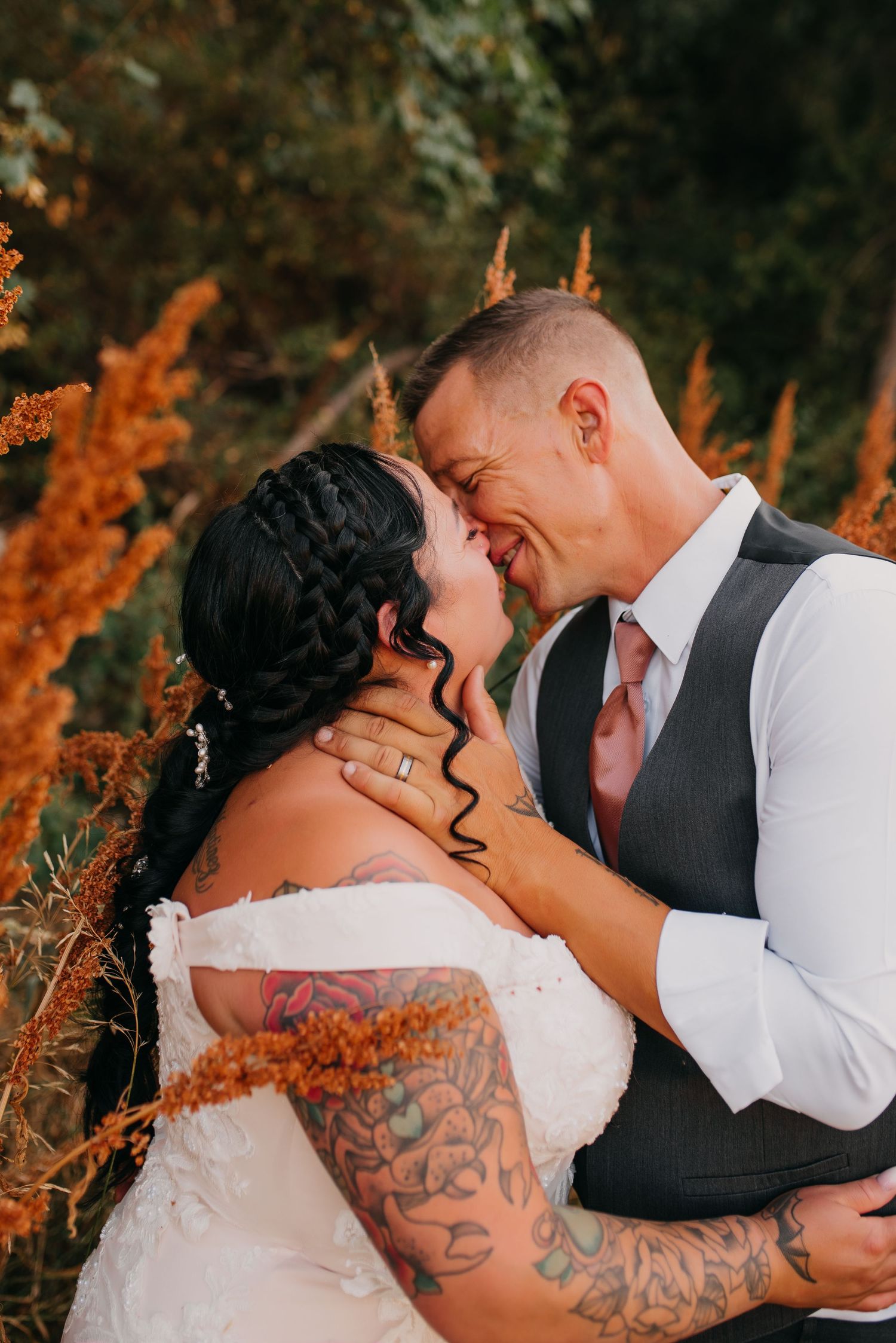 Tattooed bride and groom share an intimate moment surrounded by golden autumn foliage at sunset.