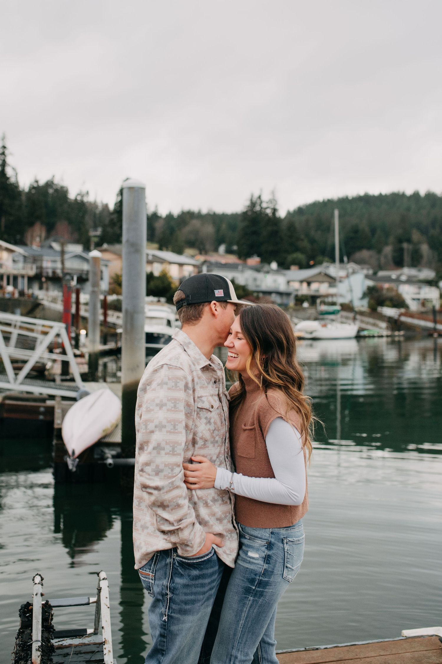 Romantic couple sharing a kiss on a wooden dock at a scenic harbor.