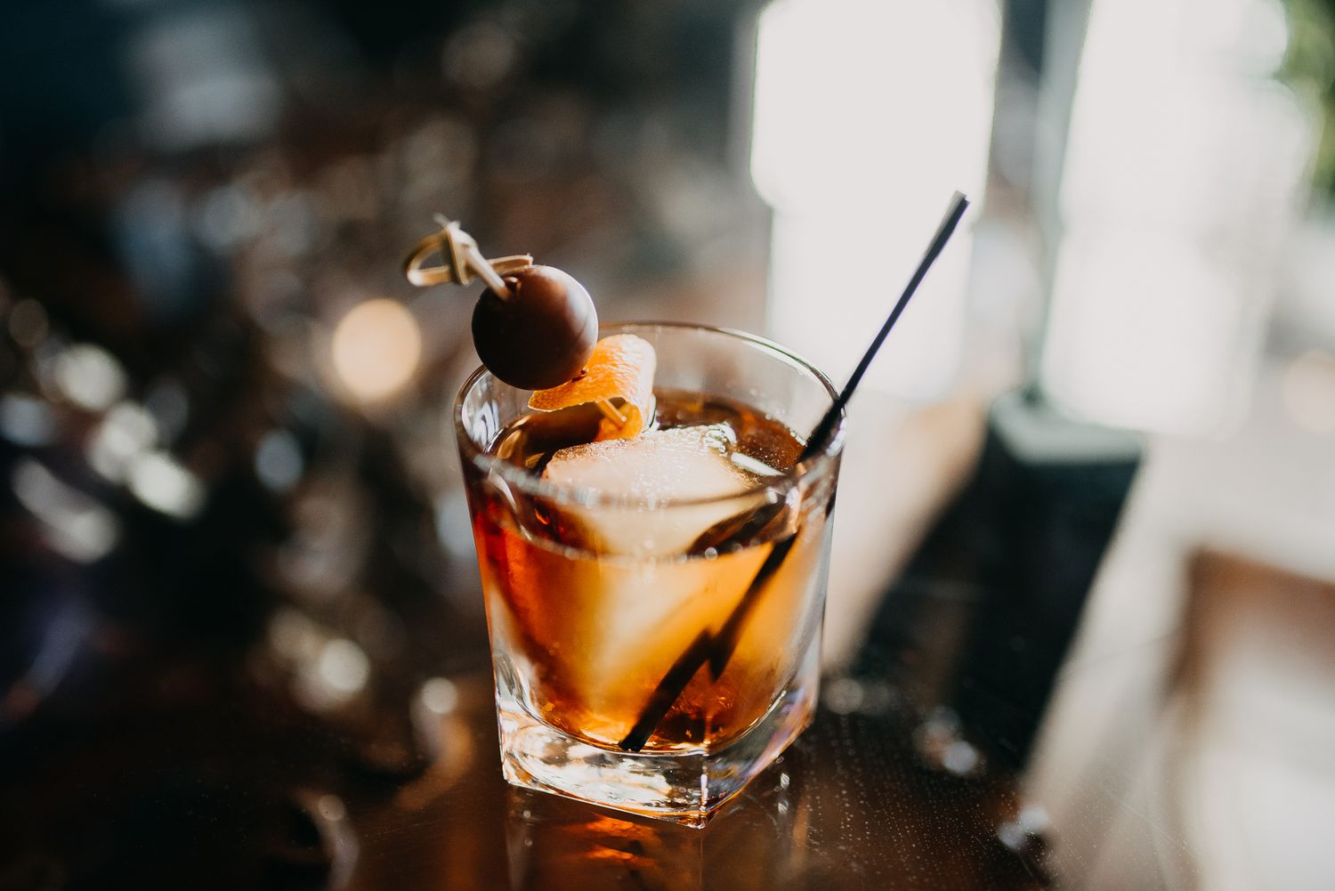 Classic Old Fashioned cocktail with cherry garnish on wooden bar surface.