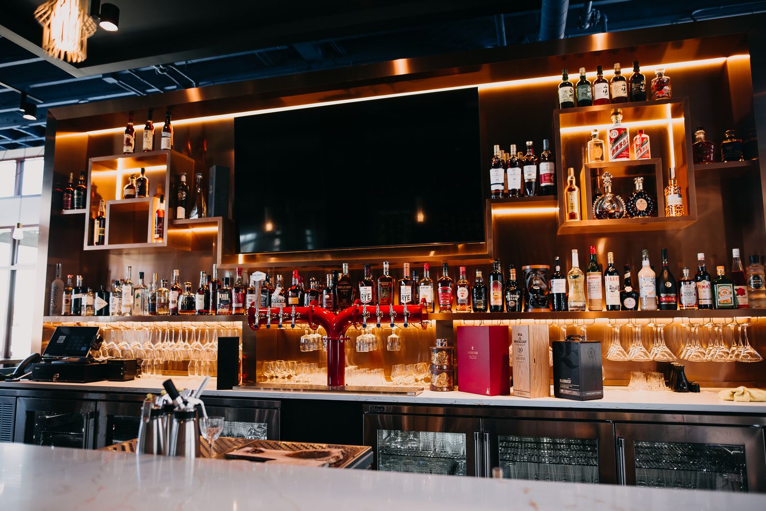 Well-stocked bar with warm lighting, shelves of spirits and glassware behind marble counter.