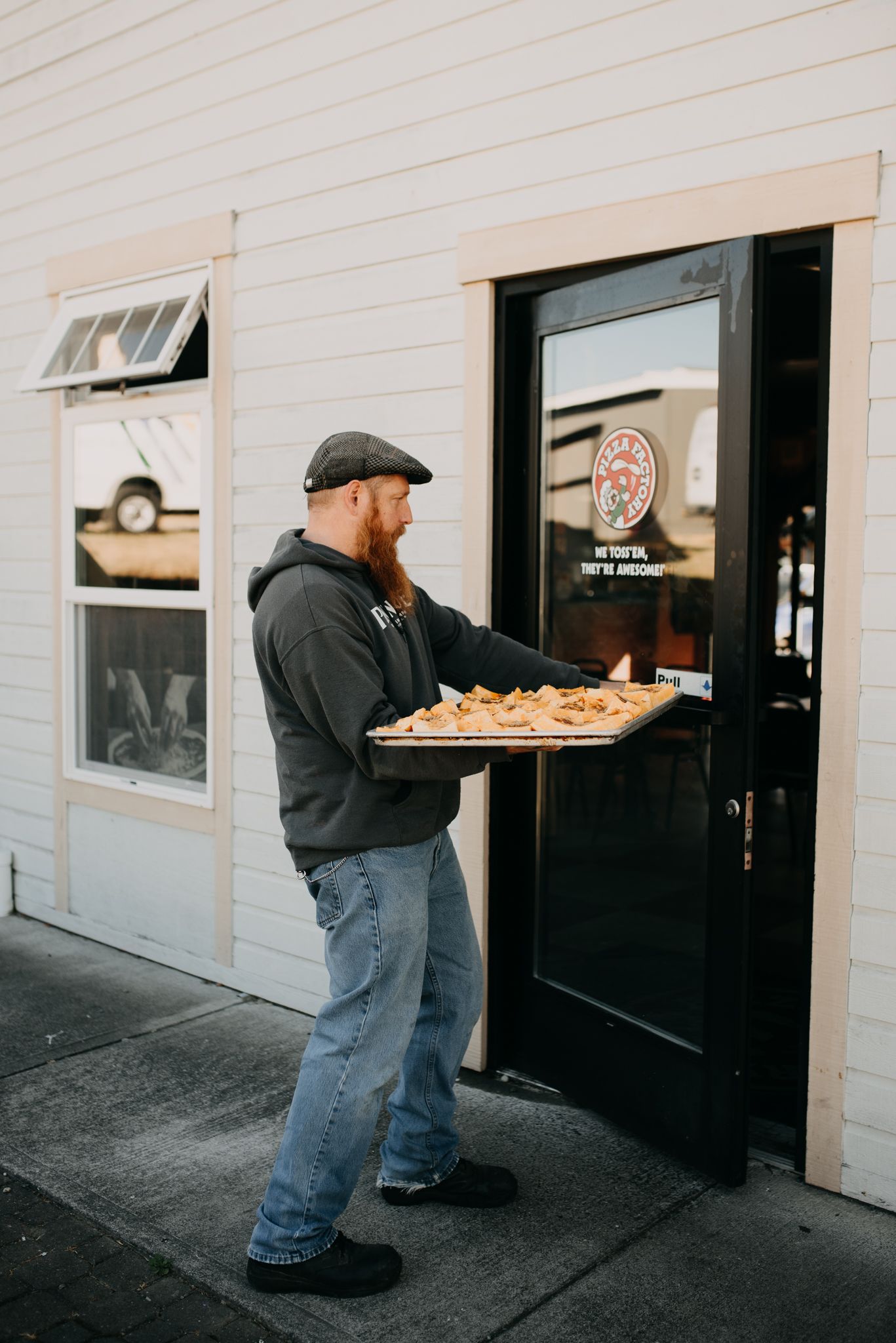 Bearded man carrying a tray of food into a restaurant entrance.
