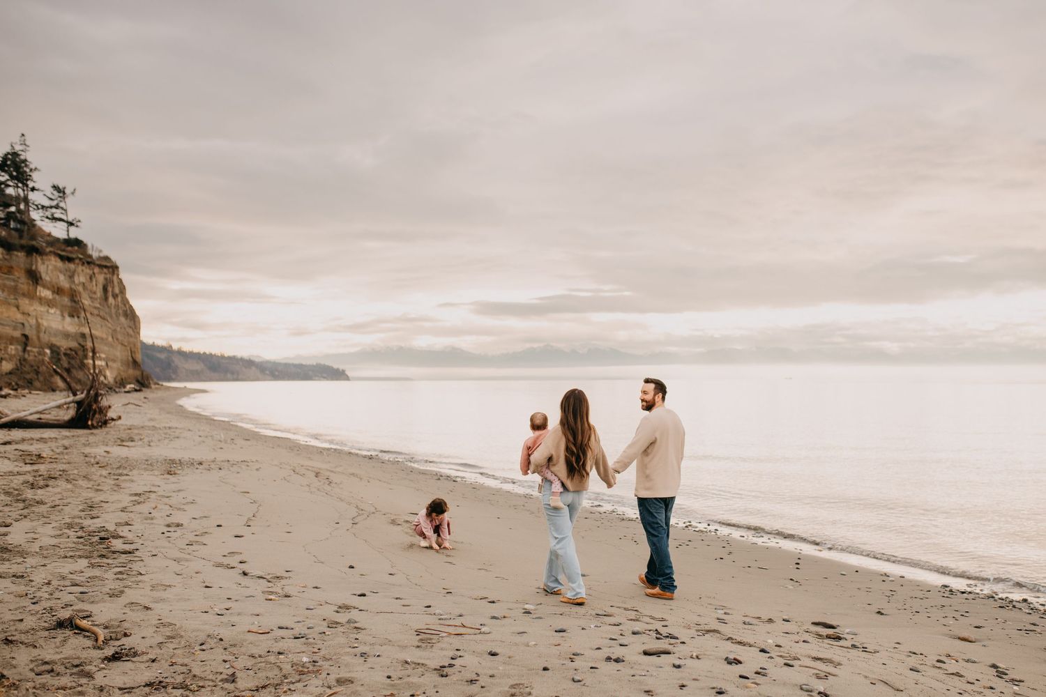 Family walking hand in hand on a sandy beach with sea cliffs in the background.