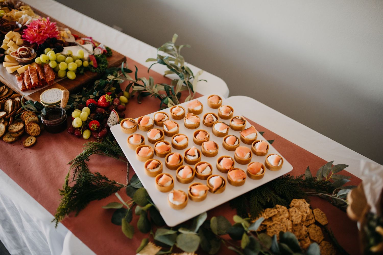 Elegant wedding reception appetizer display with smoked salmon bites, charcuterie, and fresh fruit on table.