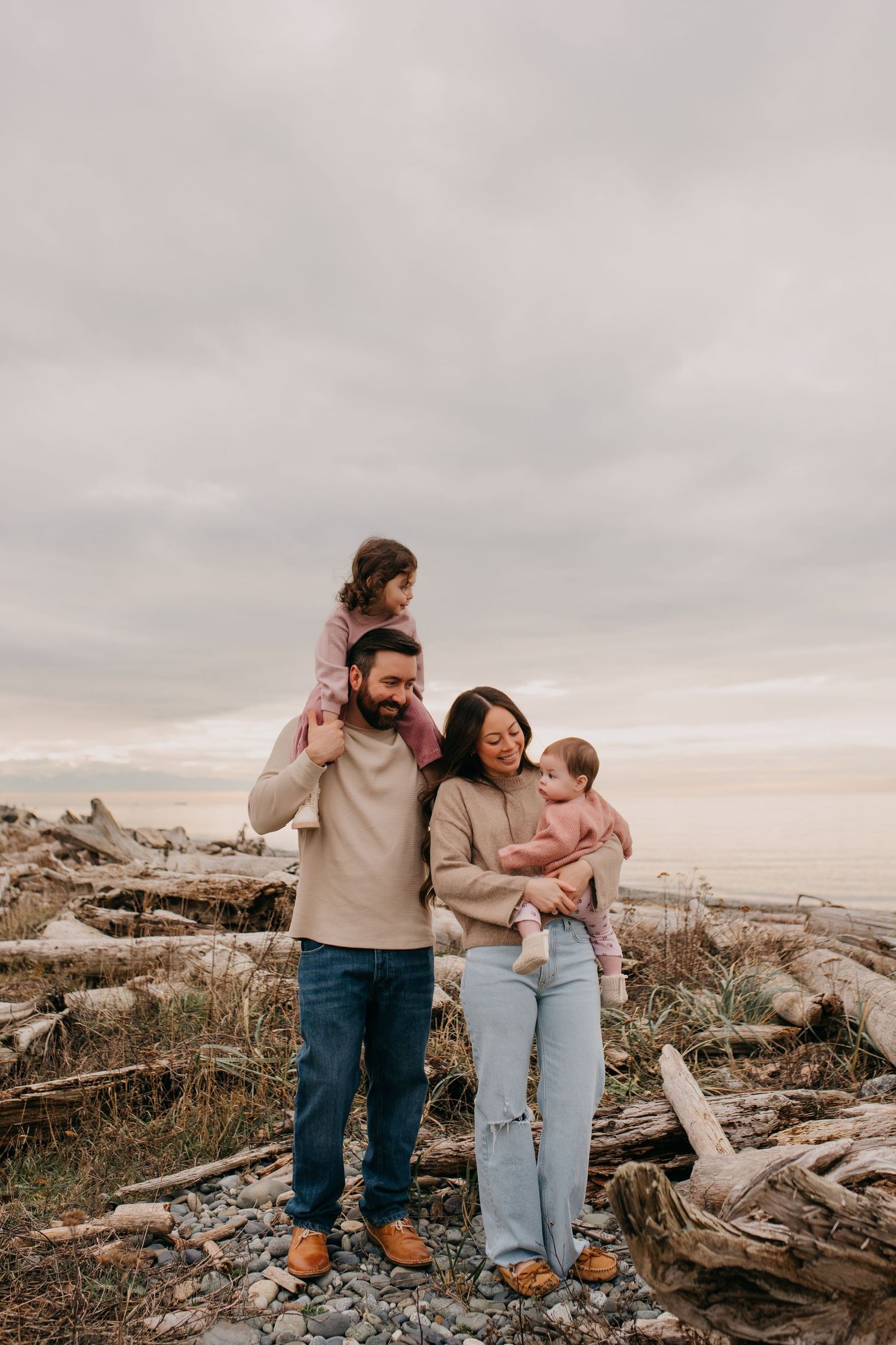 Happy family of four with two young daughters on a rocky driftwood beach.