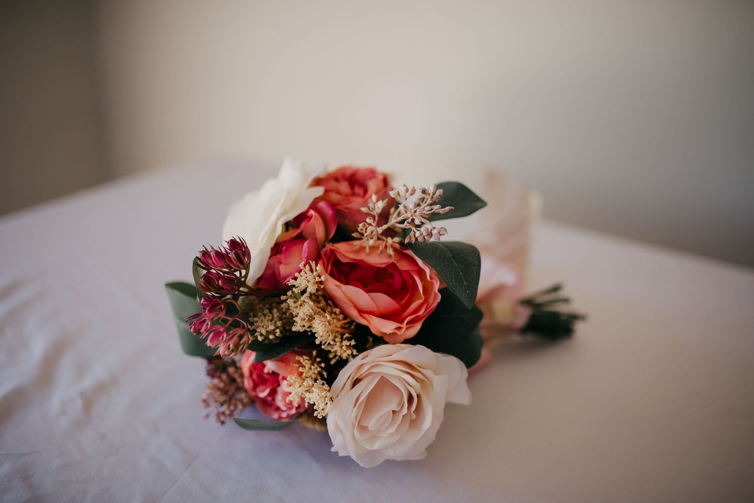 Bridal bouquet of coral and blush roses with greenery resting on a white linen surface.