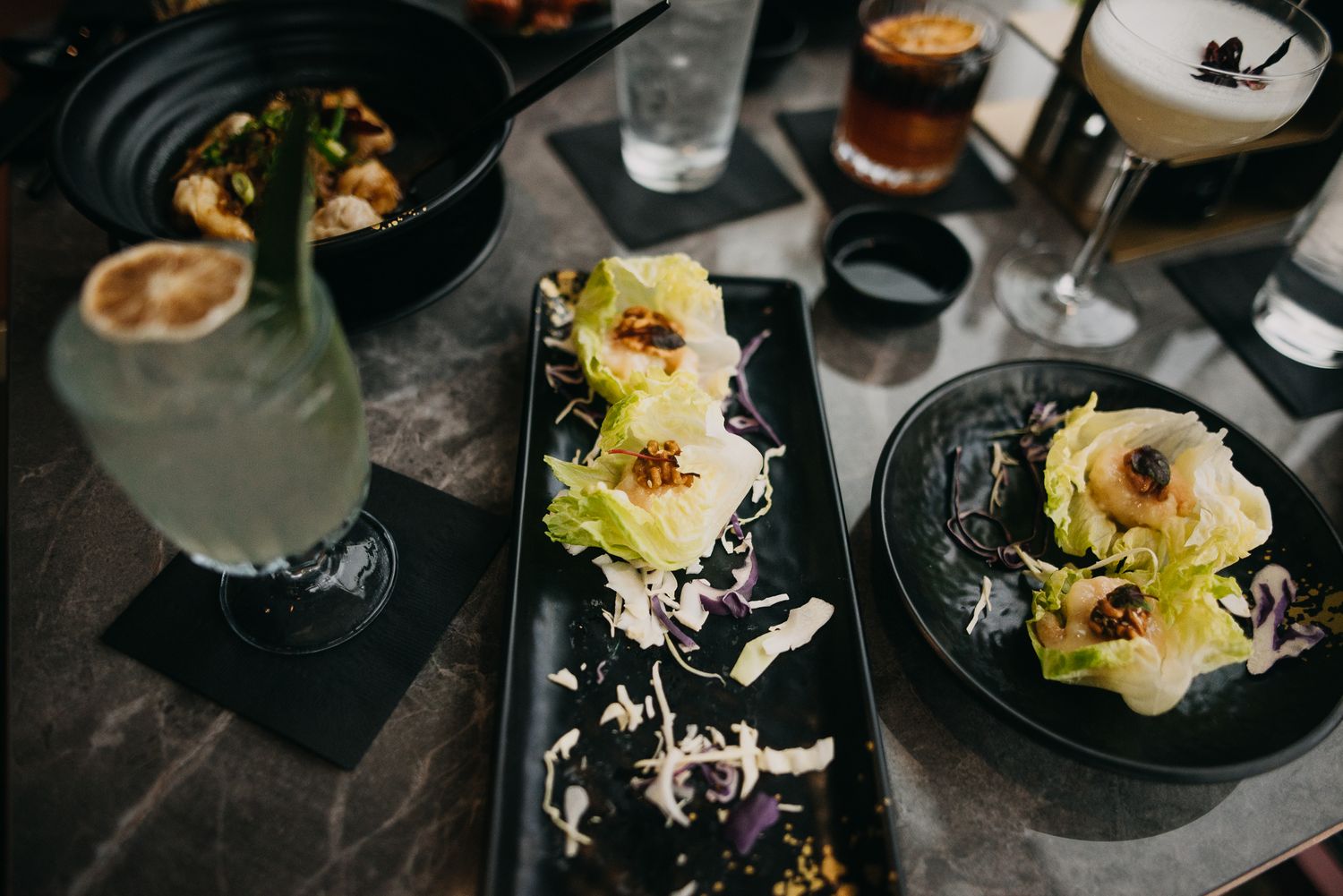Elegant appetizers with lettuce wraps and cocktails on a dark restaurant table.
