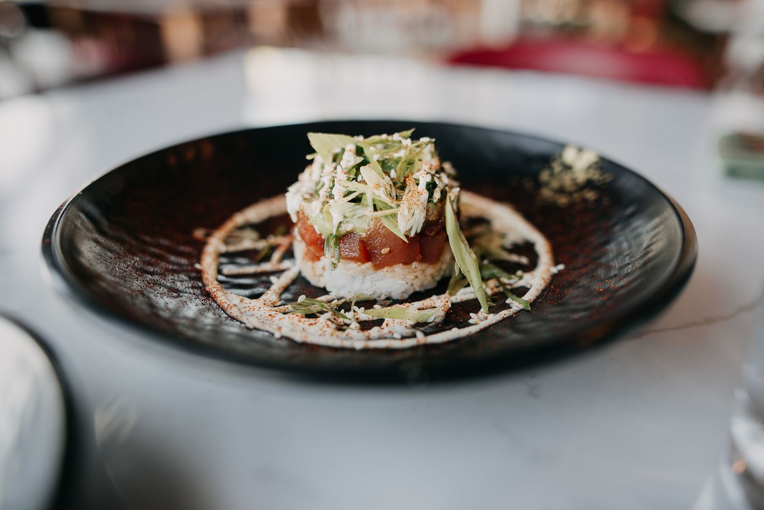 Elegant plated crab and tomato tower garnished with microgreens on dark ceramic plate.