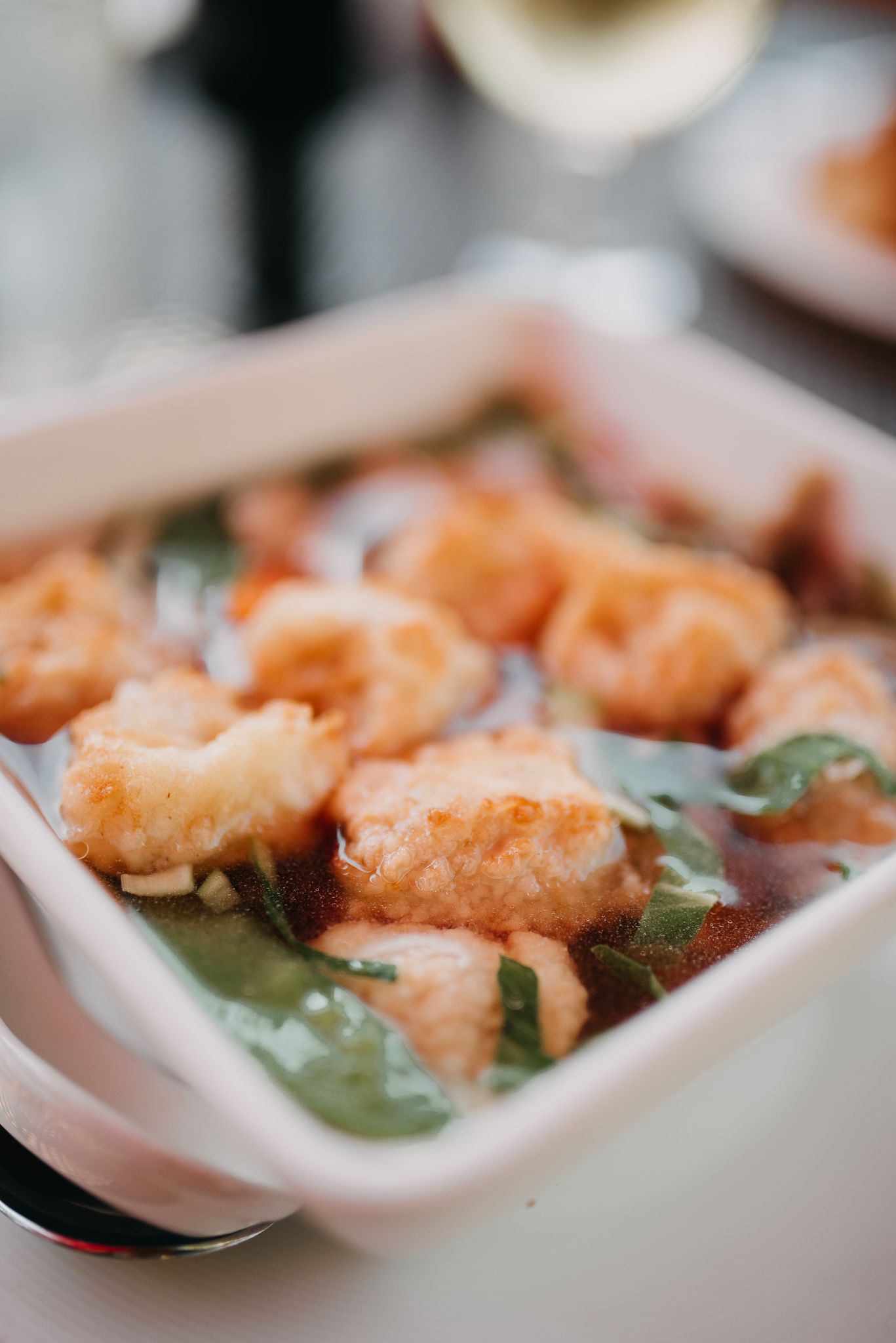 Crispy fried shrimp in tomato sauce with fresh basil in white ceramic dish.