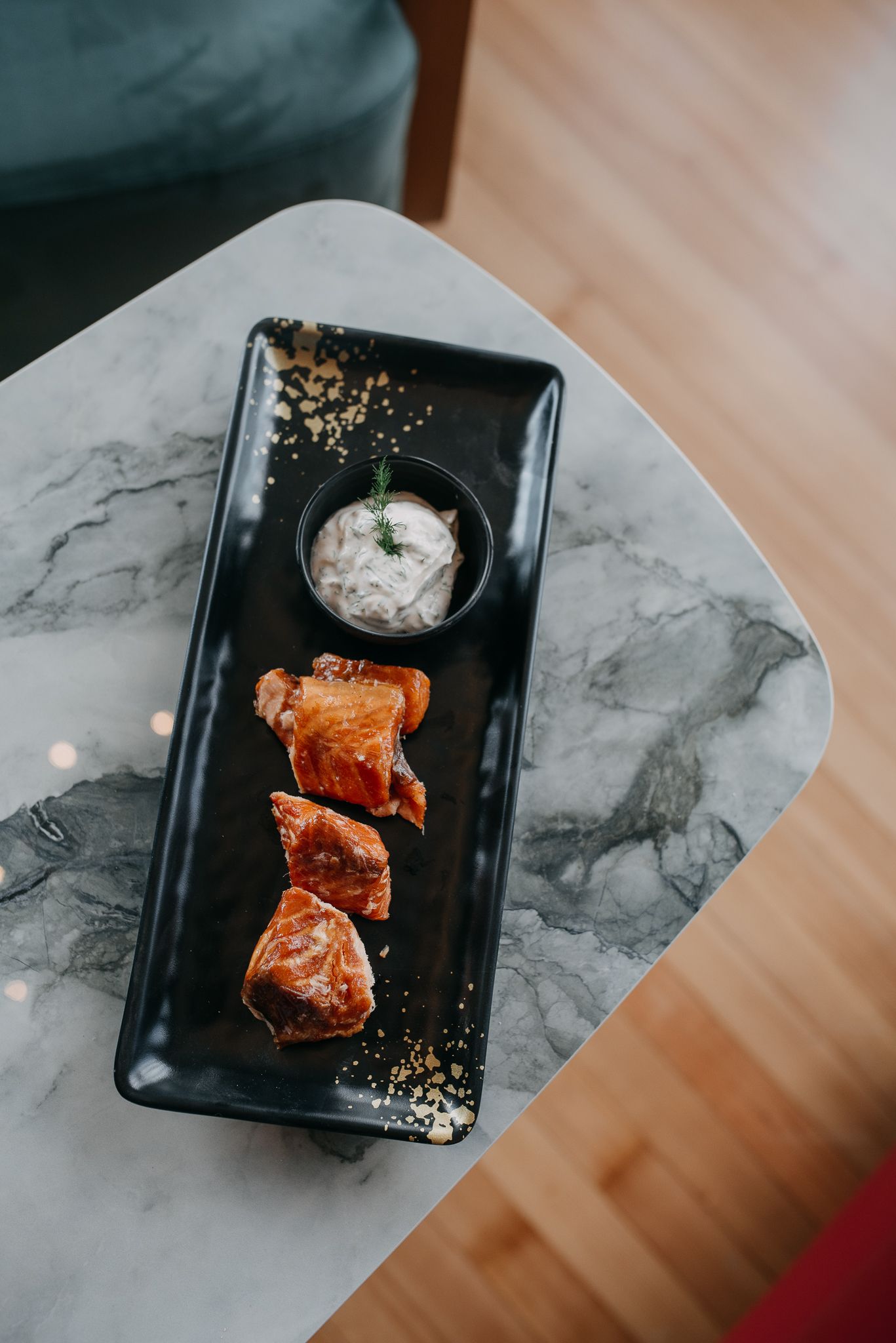 Crispy glazed chicken pieces with a creamy dipping sauce served on a black rectangular plate.