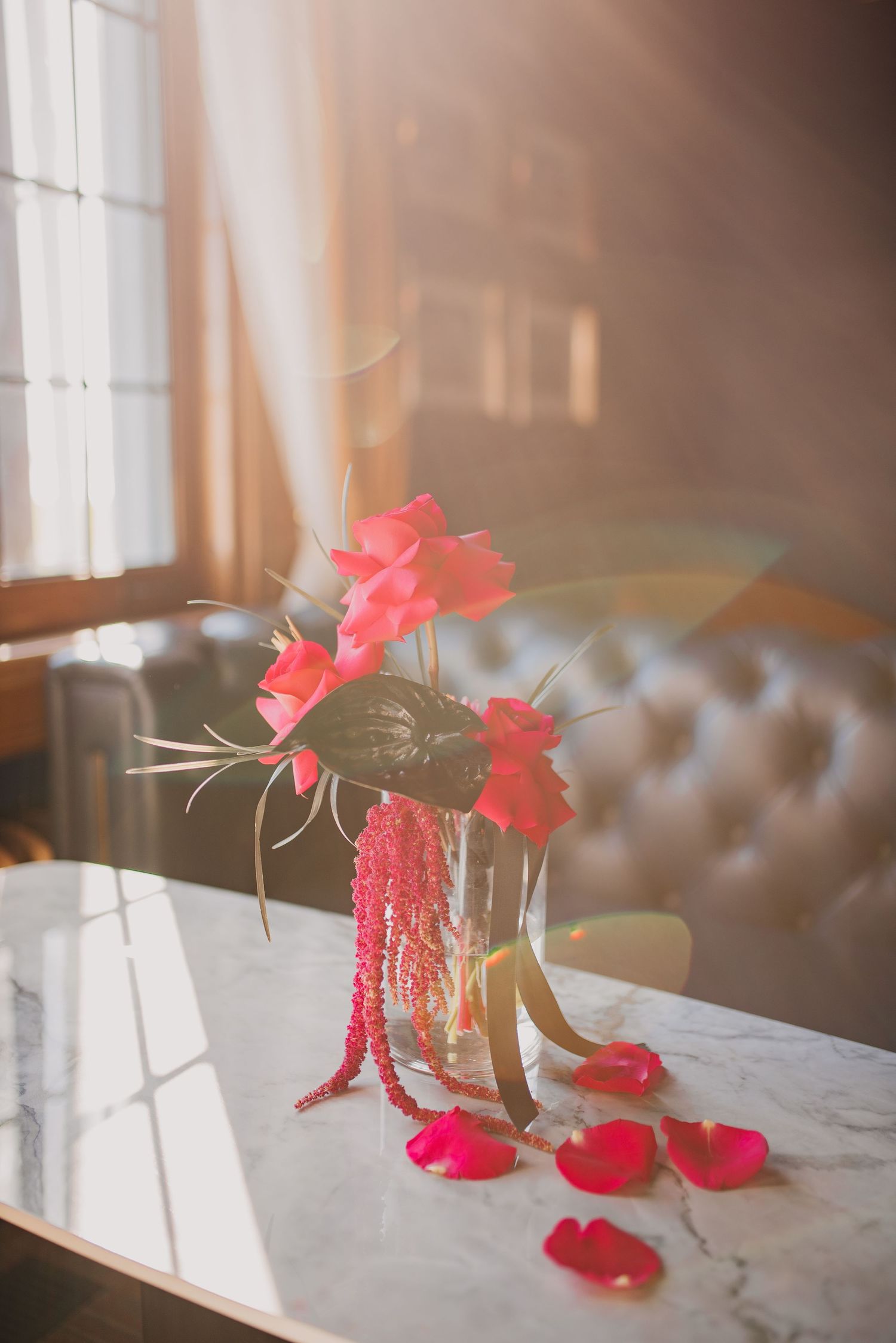 Vibrant pink tropical flowers in glass vases on a marble table with scattered rose petals.