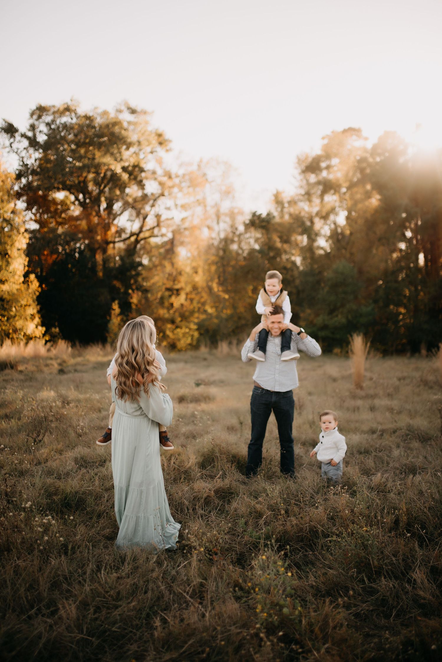 Family of four in golden autumn field with father carrying child on his shoulders.