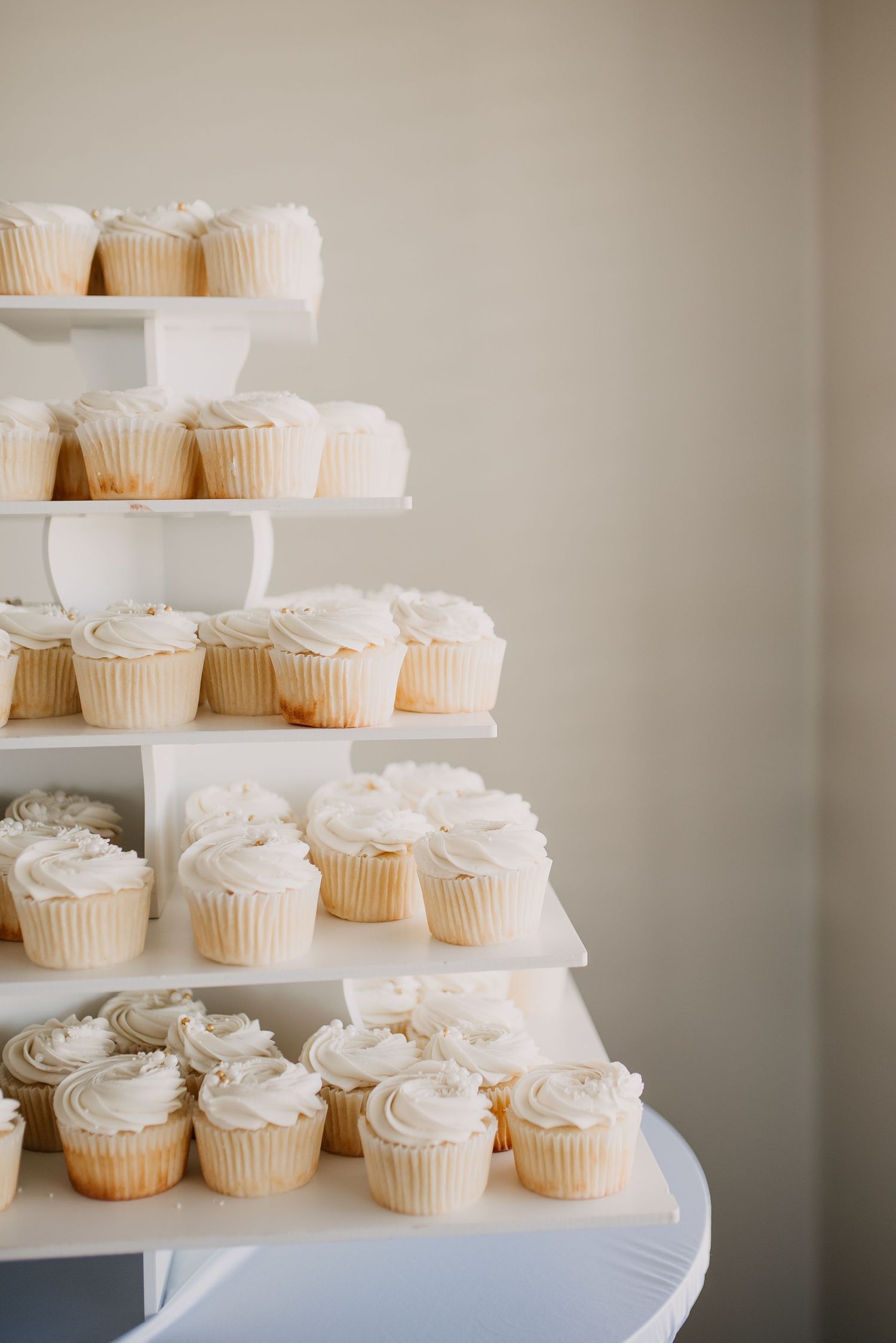 Elegant five-tier white cupcake tower display with swirled vanilla frosting for a wedding reception.