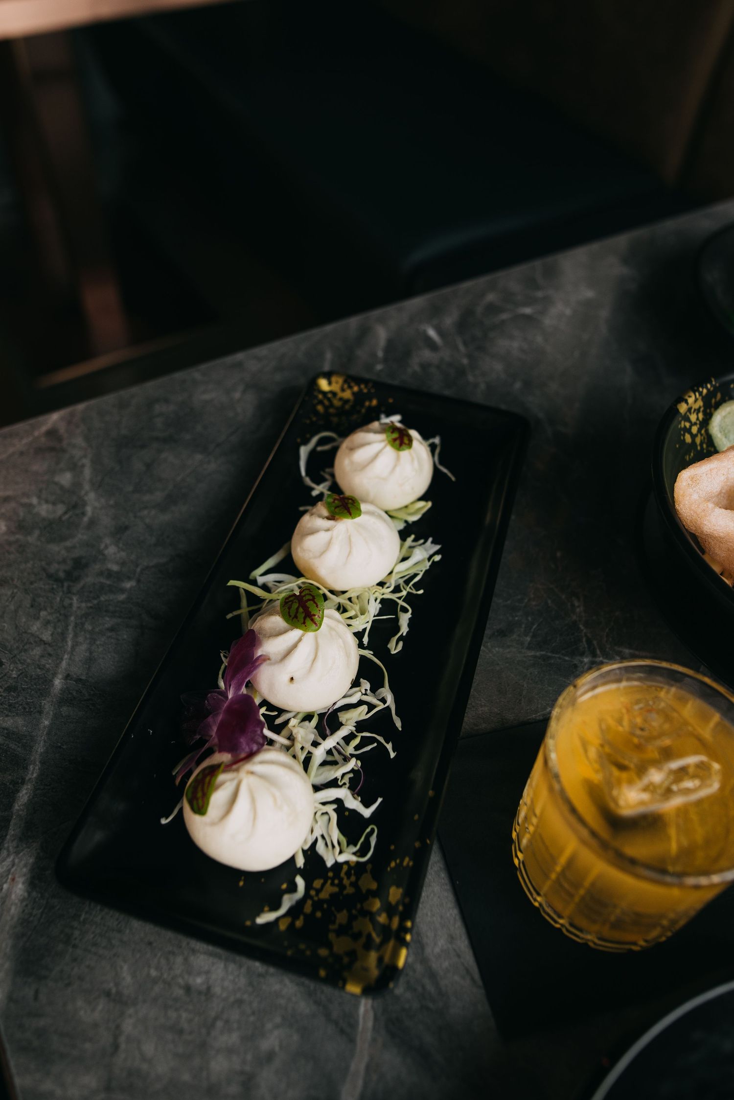 Four steamed bao buns with shredded cabbage and purple onion on a black rectangular plate.