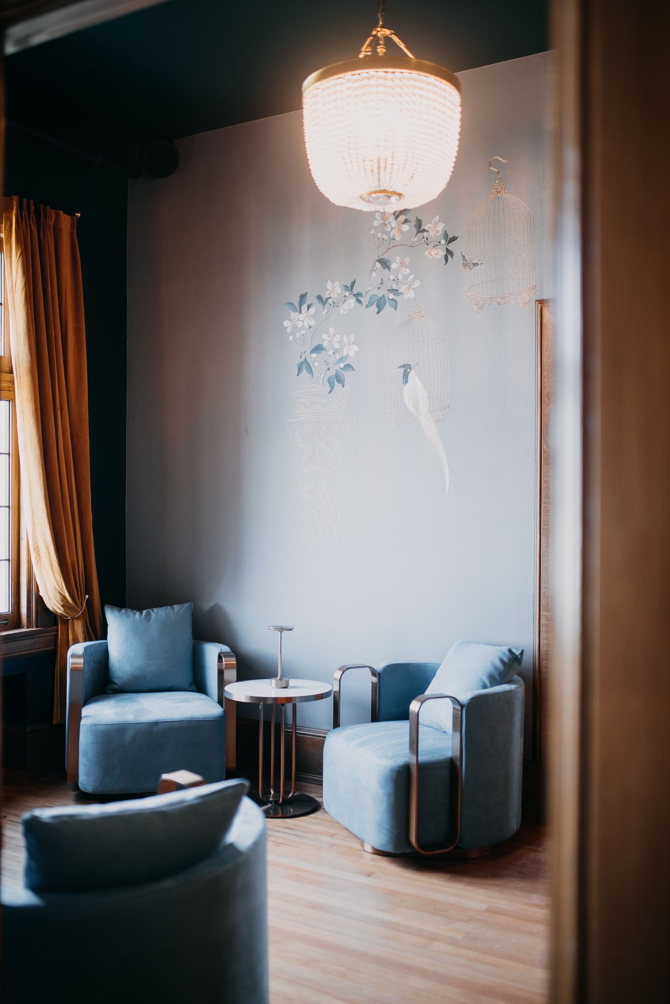 Elegant lounge seating area with blue velvet chairs and floral wall mural.