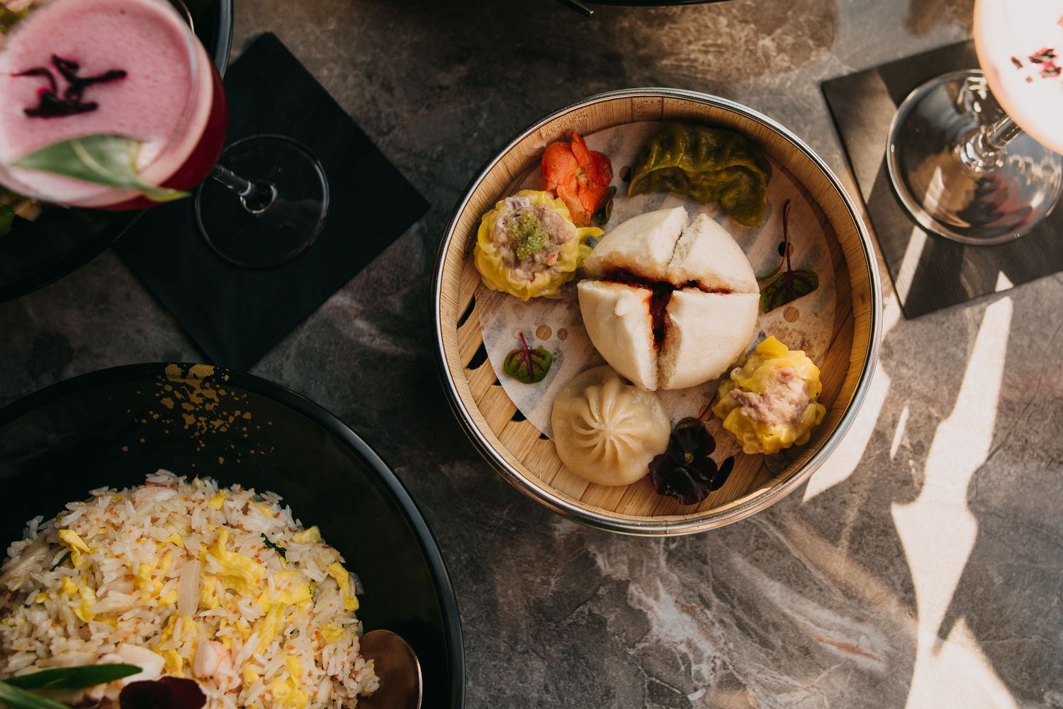 Assorted colorful steamed dim sum buns in a bamboo steamer basket with fried rice on the side.