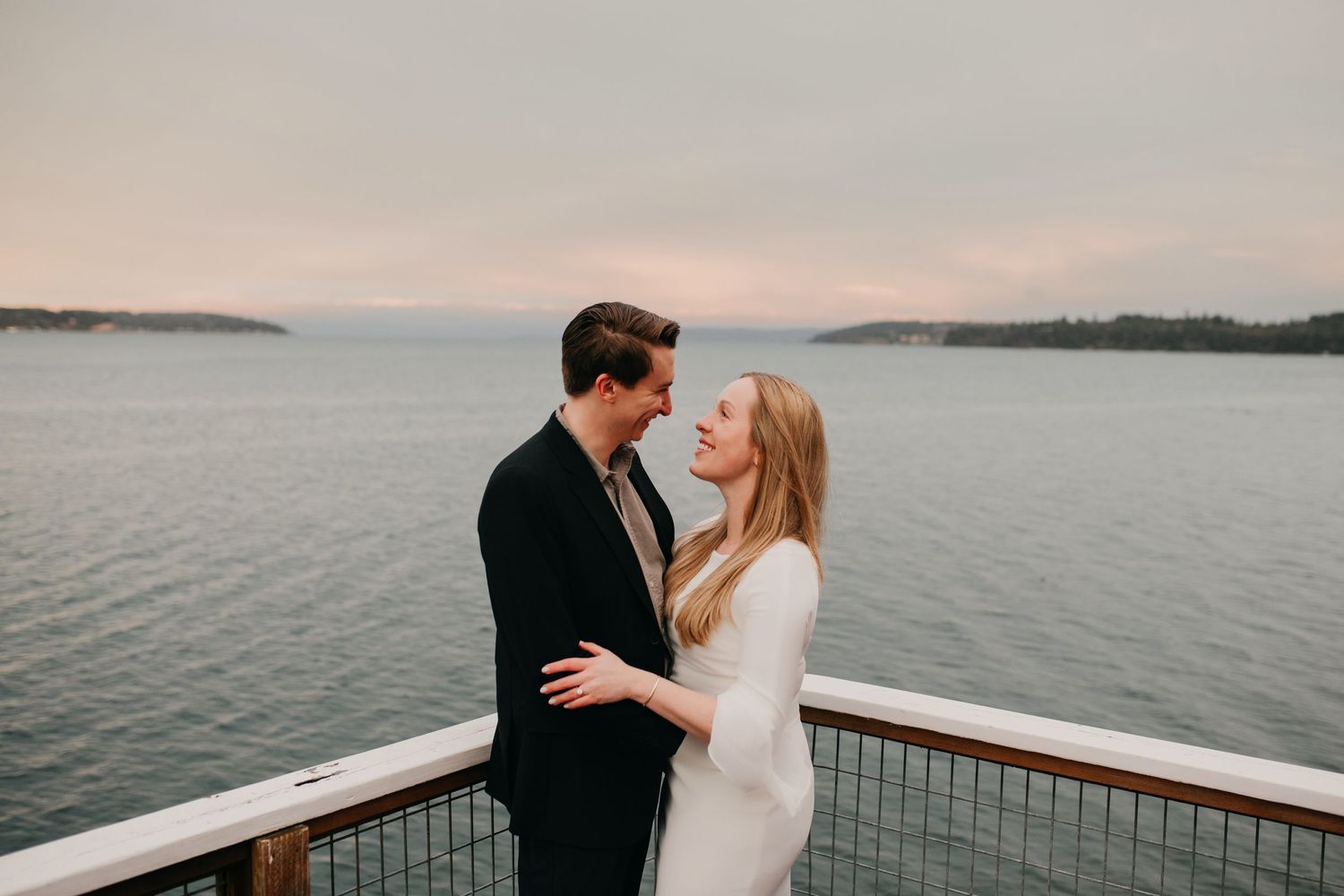 Romantic couple embracing on waterfront deck at sunset with scenic island views in the background.