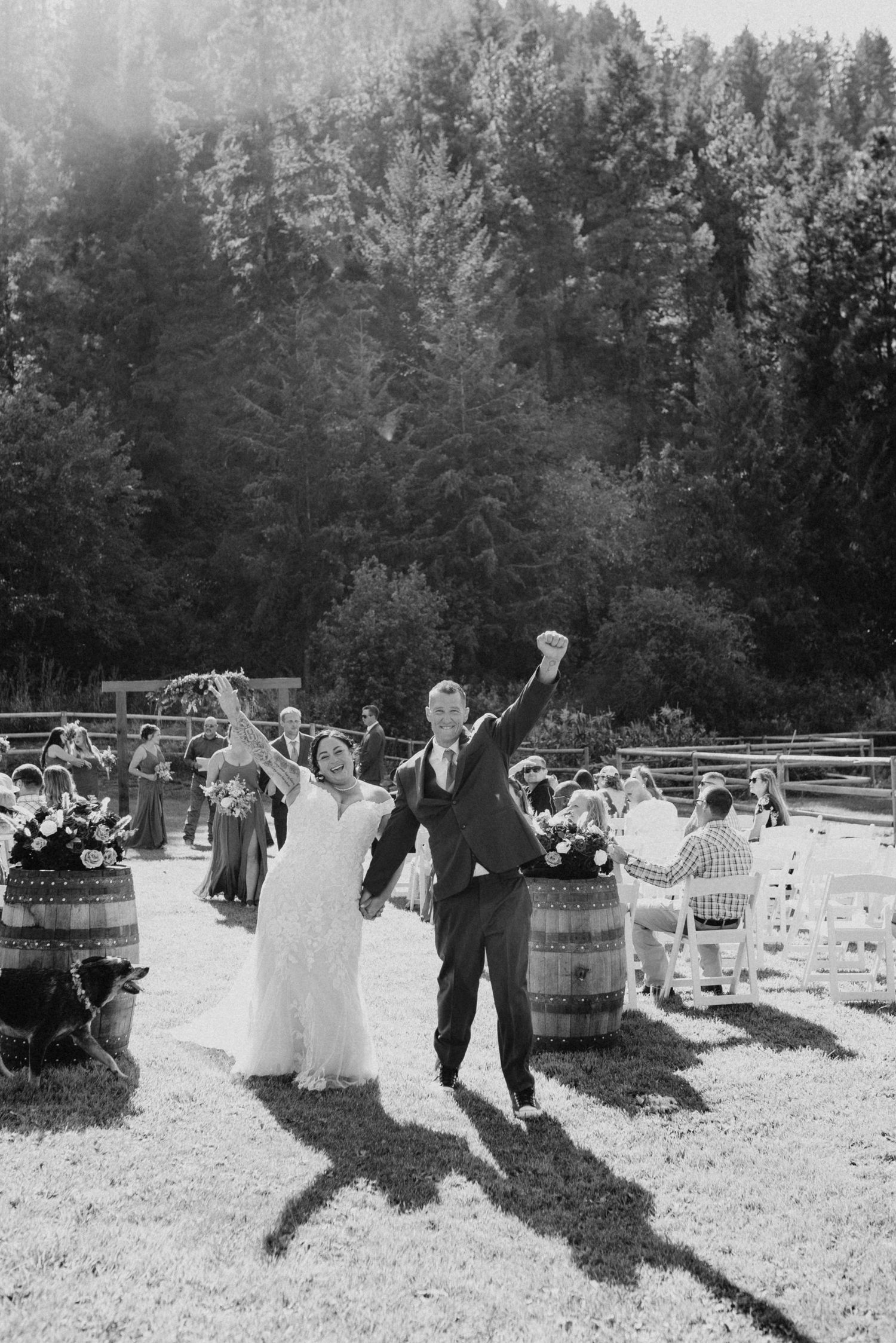 Joyful newlyweds celebrate their recessional with raised arms at an outdoor rustic barn wedding ceremony.