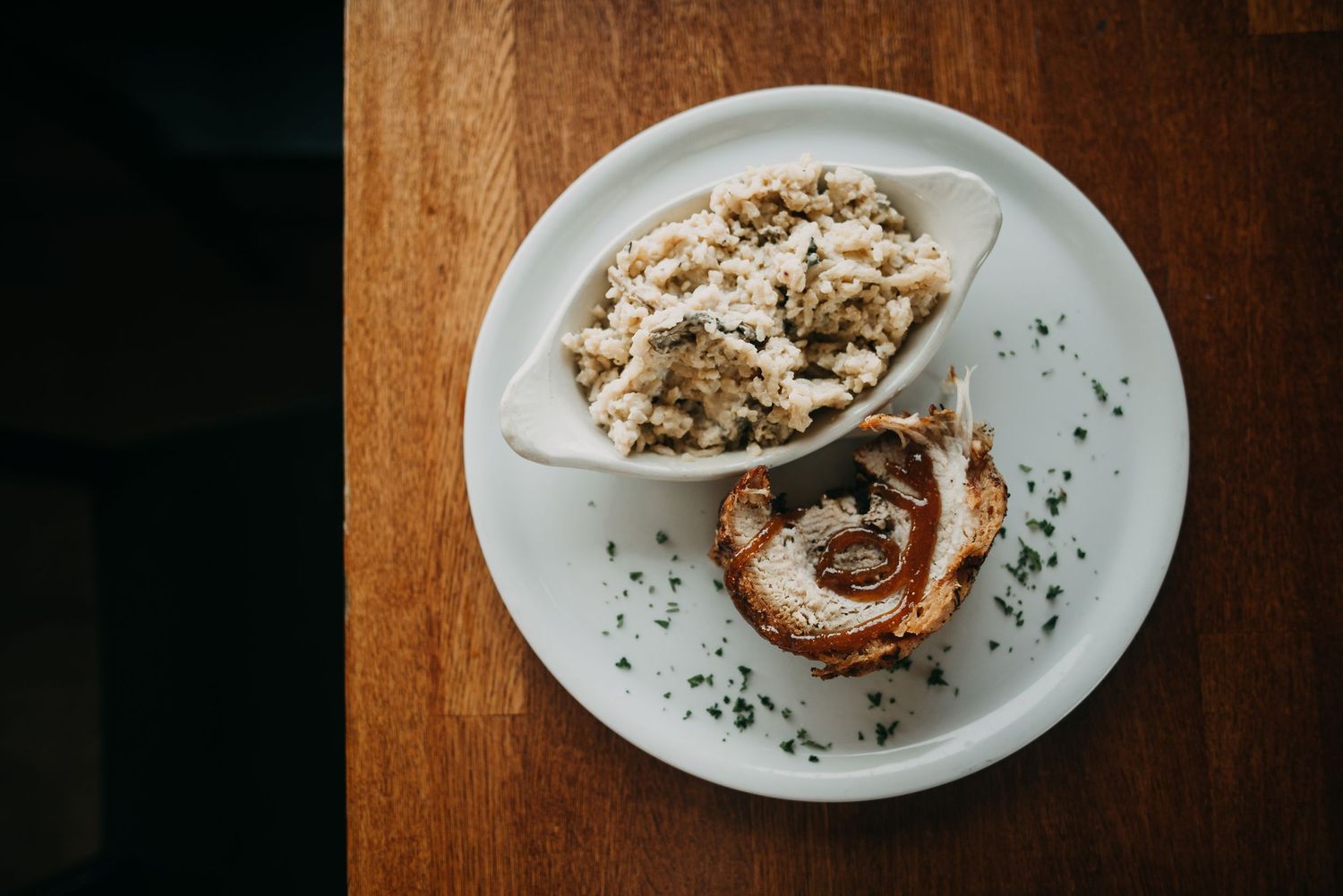 A white plate with creamy mushroom risotto and a golden-brown rolled pork dish garnished with herbs.