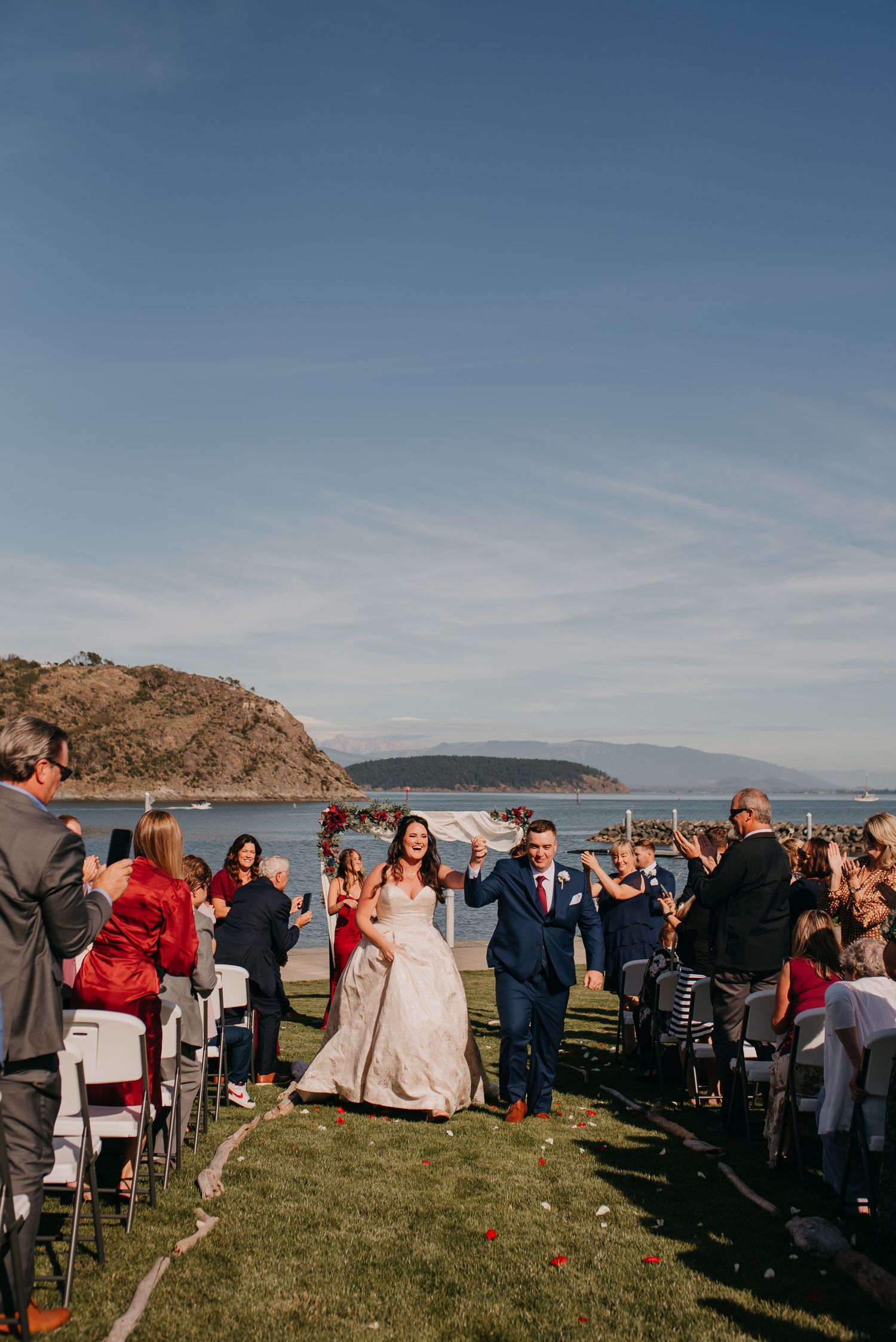 Bride and groom celebrate recessional with guests at outdoor waterfront wedding ceremony.