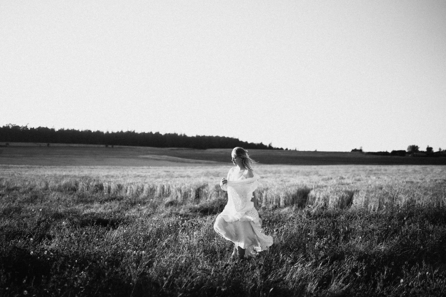 Black and white photo of a bride in a white dress running through an open field.