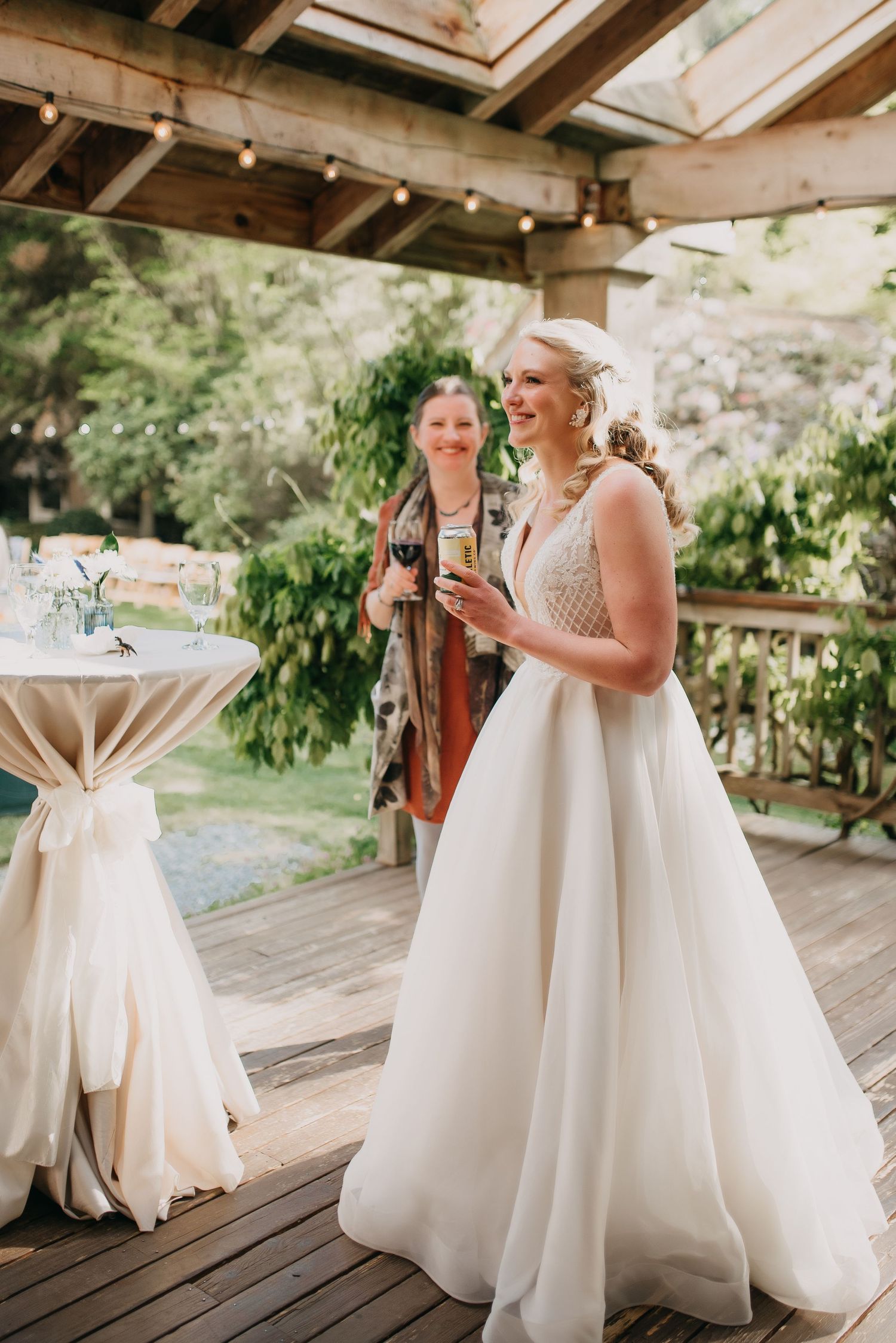 Radiant bride in ball gown holds champagne glass on decorated outdoor deck with string lights.