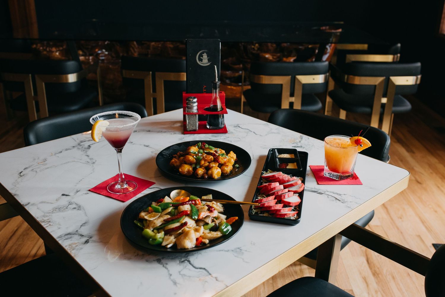 Assorted Asian dishes and colorful cocktails on a marble table in a modern restaurant.