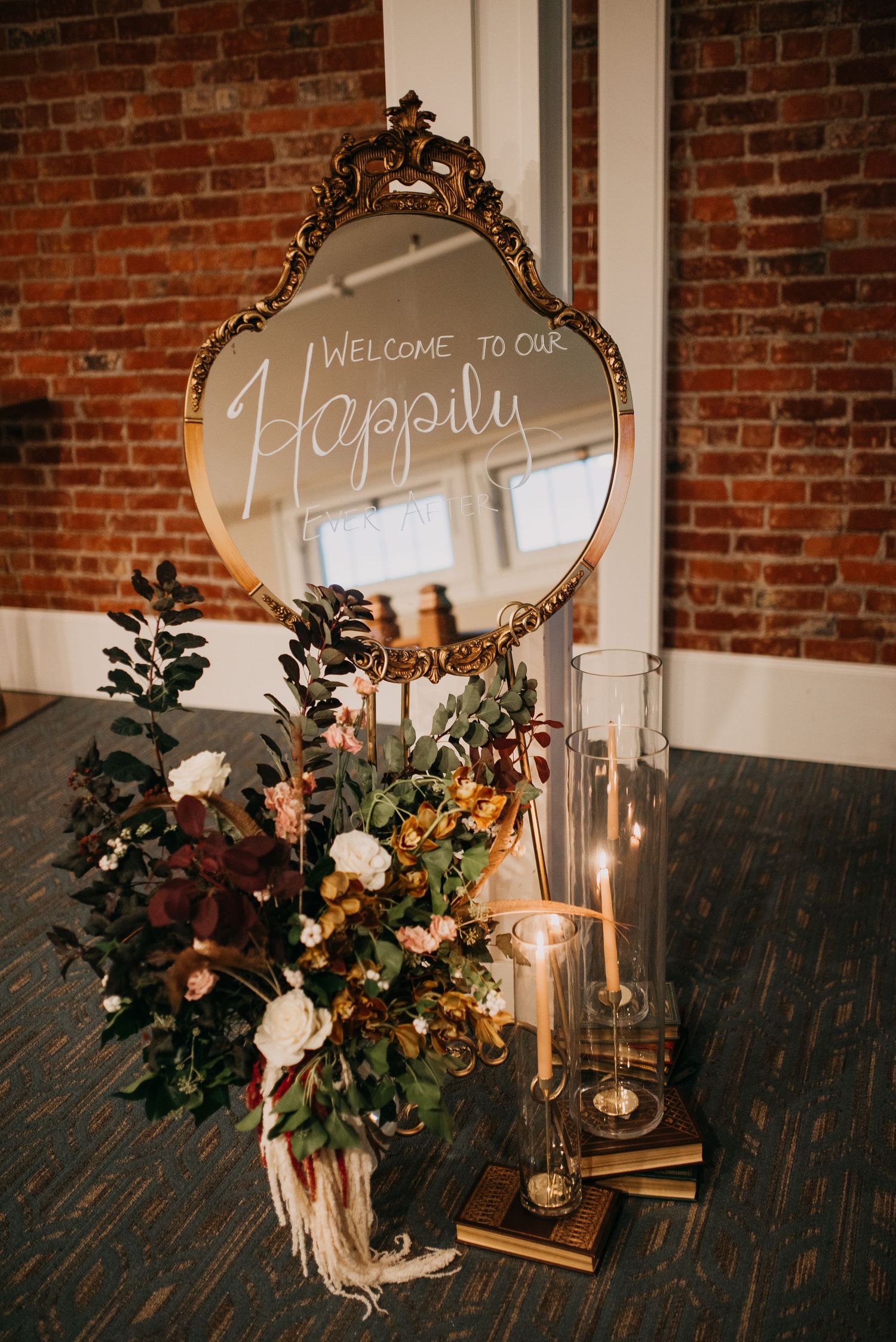 Gold ornate mirror with Welcome to Our Happily sign displayed with candles and autumn florals.