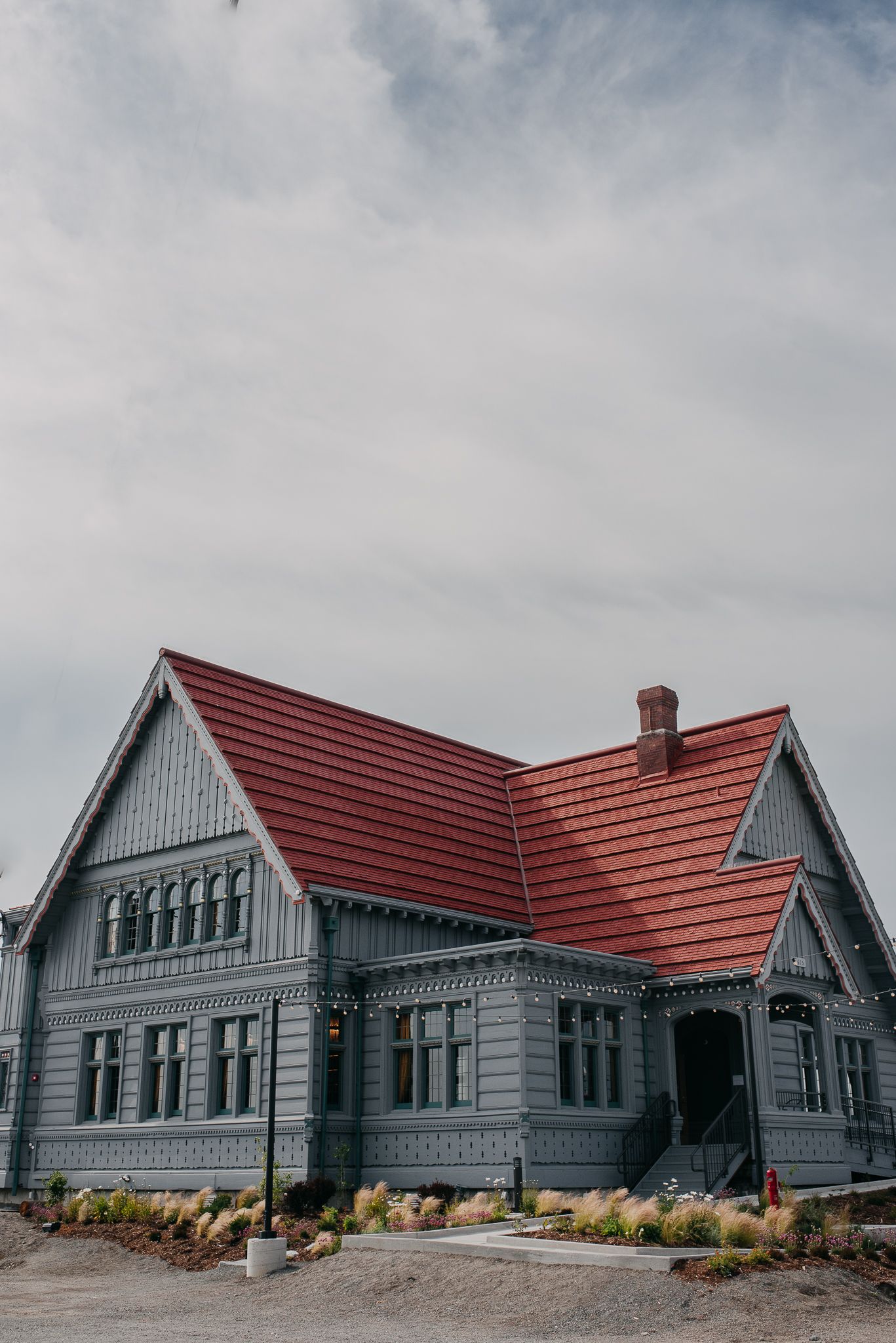 Historic gray Victorian house with ornate trim and red roof under cloudy sky.