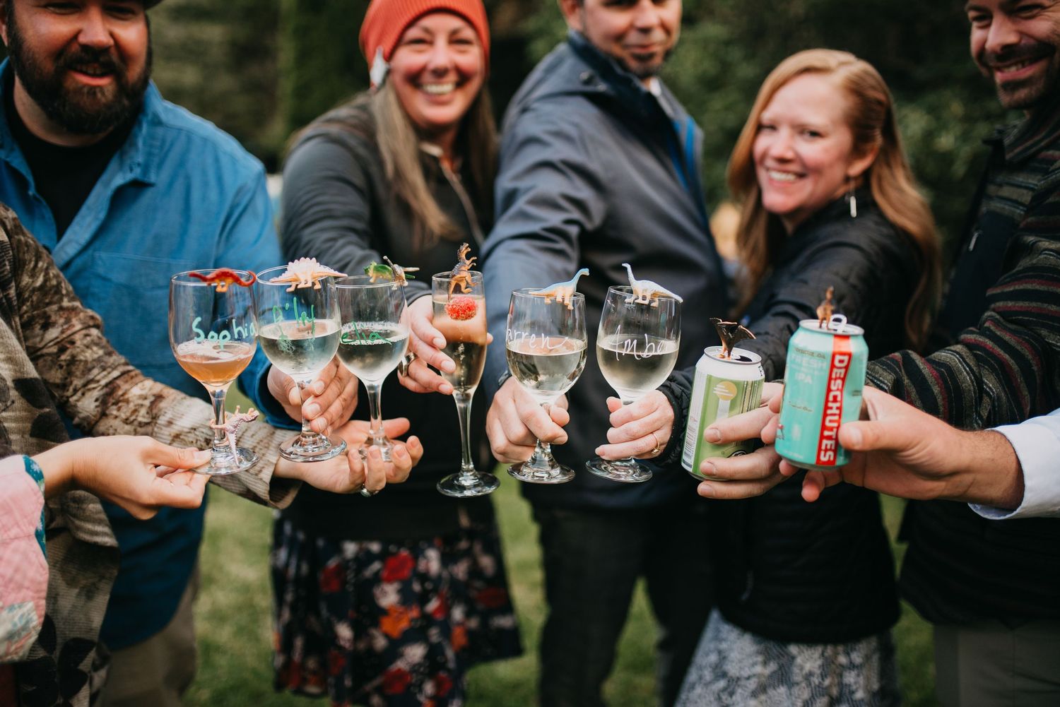 Wedding guests joyfully clink glasses of wine and craft beer in an outdoor celebration toast.