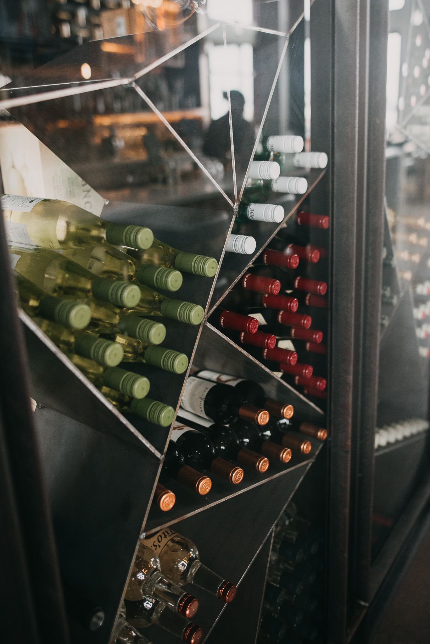 Wine bottles stored in diagonal rack inside glass display case at restaurant.