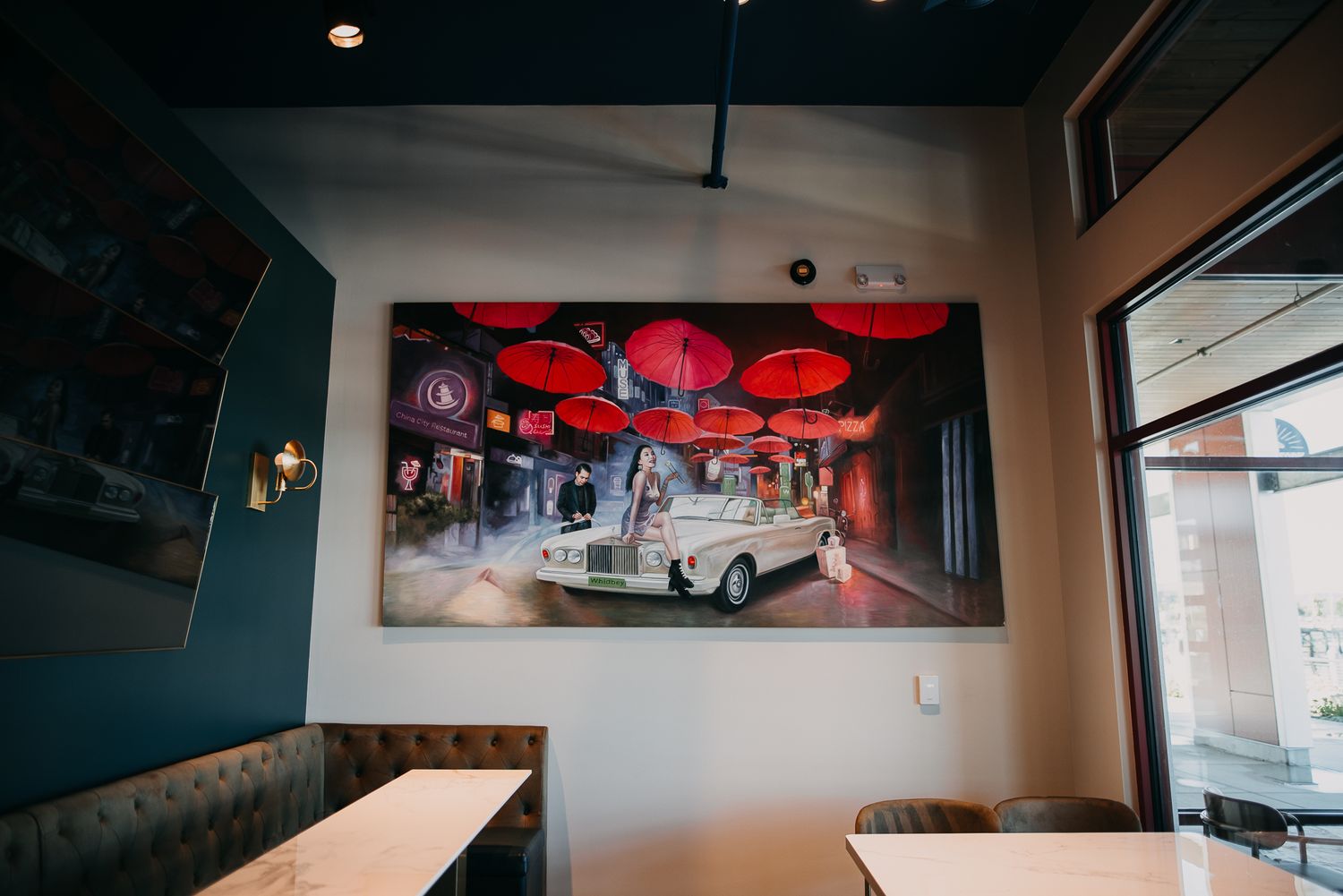 Cozy restaurant interior with a large mural of red umbrellas and a vintage car on the wall.
